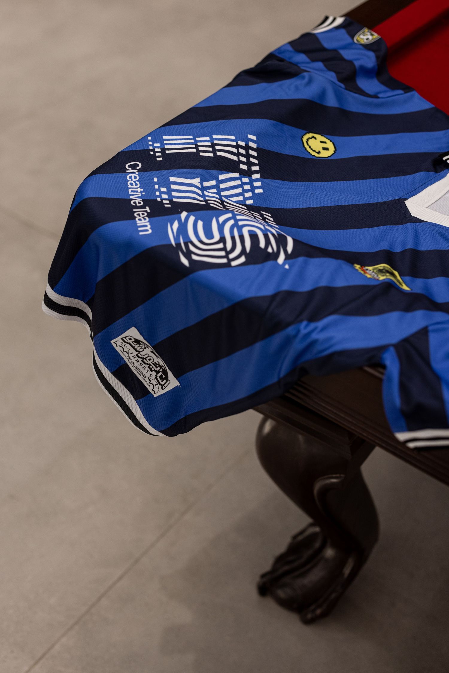 Blue and black striped soccer jersey draped over a dark wood pool table leg on a gray floor.