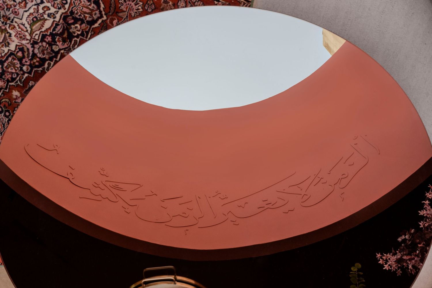 Terracotta ceiling dome with intricate Arabic calligraphy carved in relief against a white oval center.
