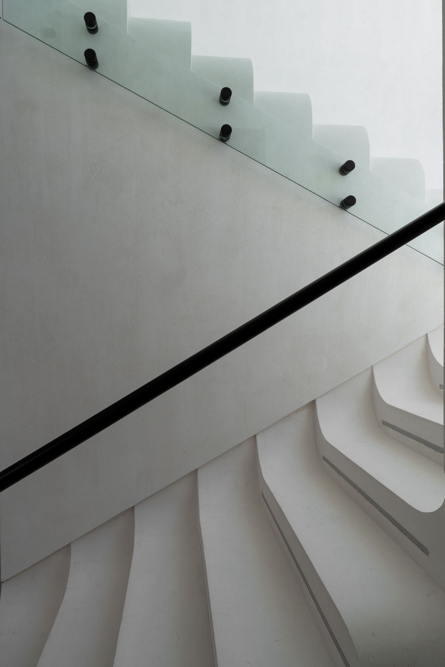 Architectural white sculptural staircase with glass railing and black metal bolts from above.