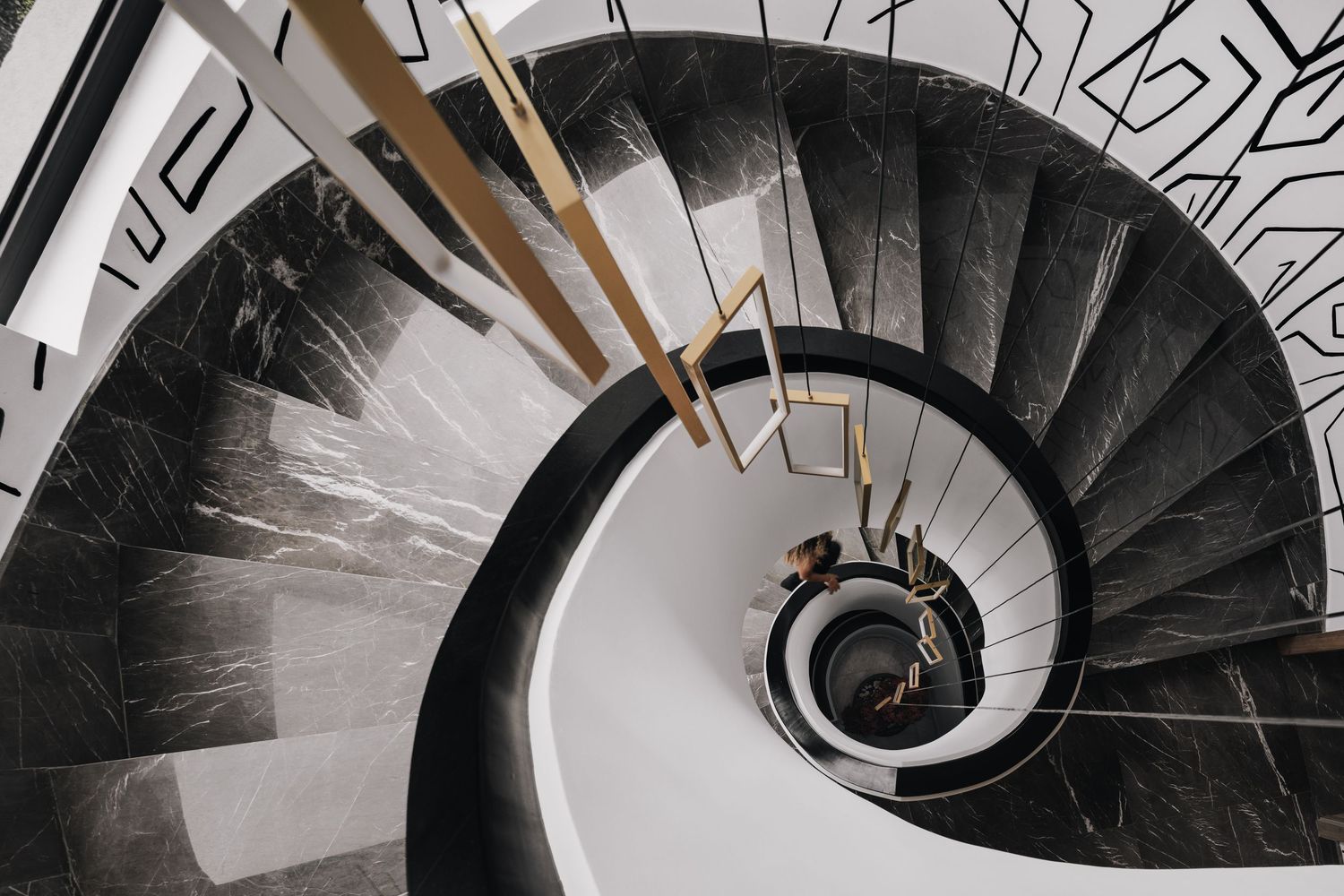 Aerial view of elegant spiral staircase with dark marble steps, gold railing accents, and bold graphic wall mural.