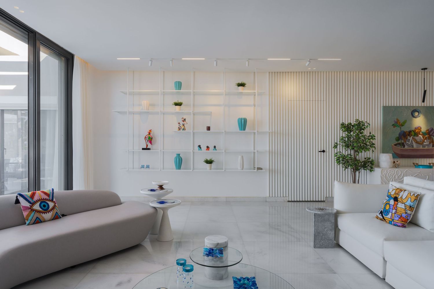 Bright contemporary living room with white built-in shelves, colorful decor, marble floors, and two sofas.