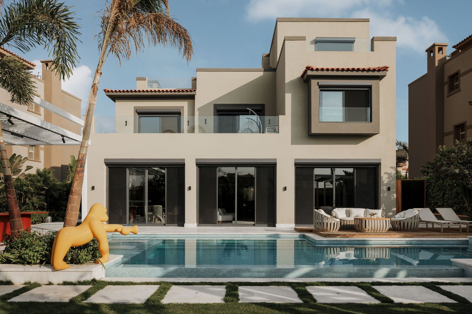 Luxury two-story villa with private swimming pool, yellow horse sculpture, and palm tree garden.
