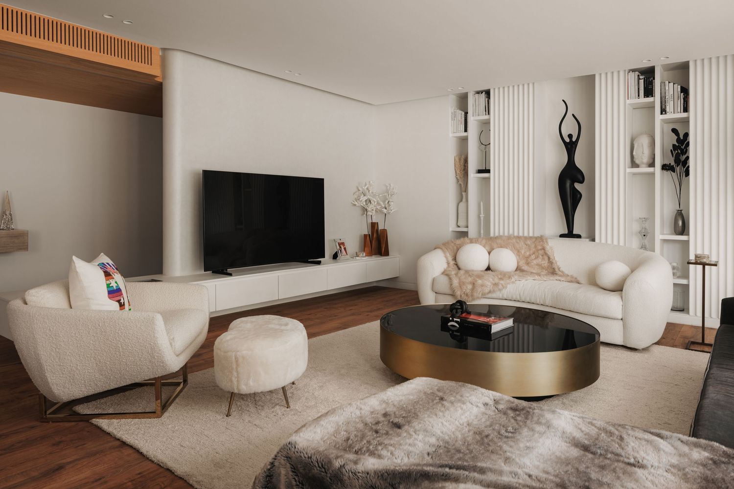 Modern living room with white bouclé sofas, gold coffee table, black TV unit, and decorative sculpture on hardwood floors.
