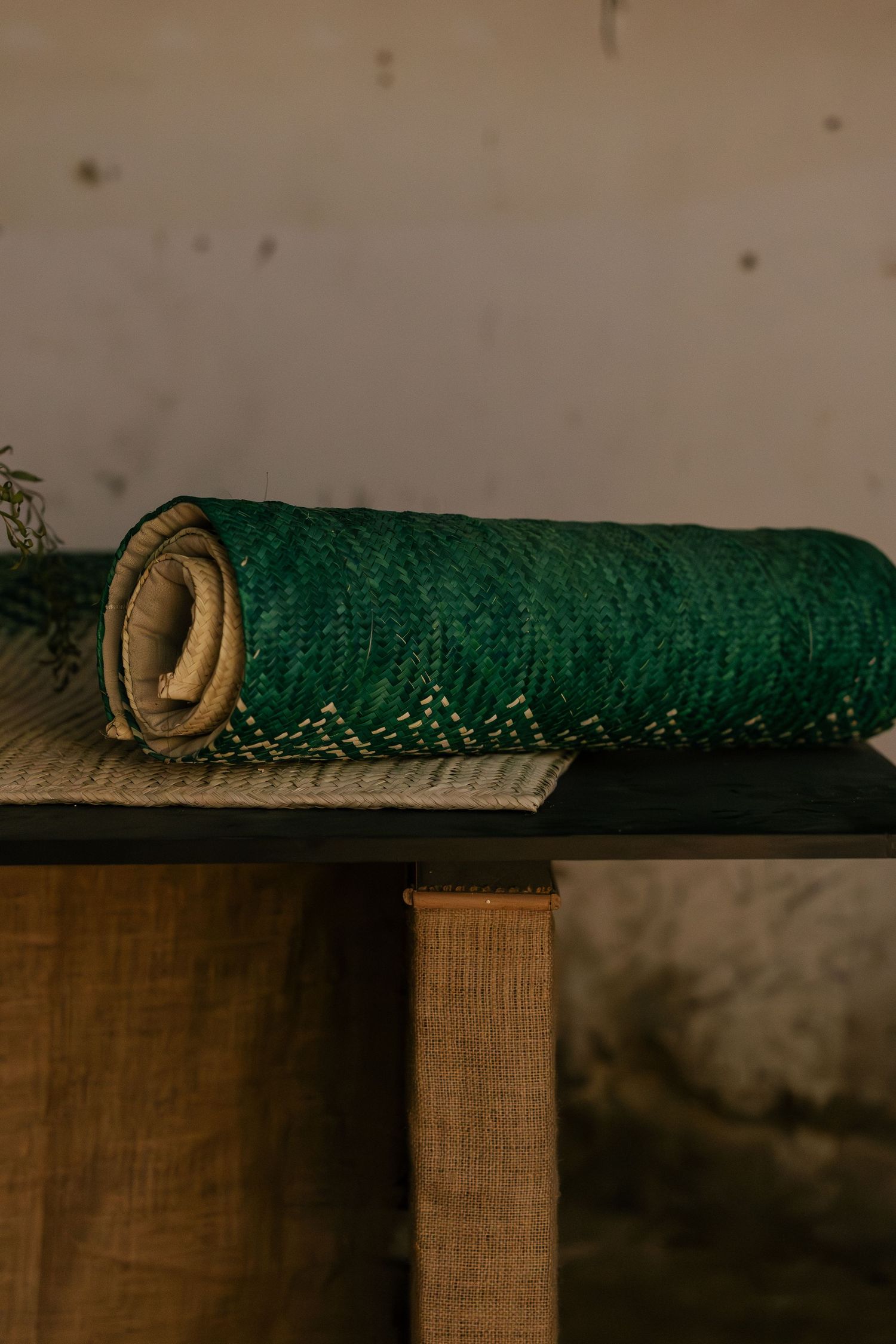 Rolled green and beige woven textile mat displayed on a wooden table in a rustic setting.
