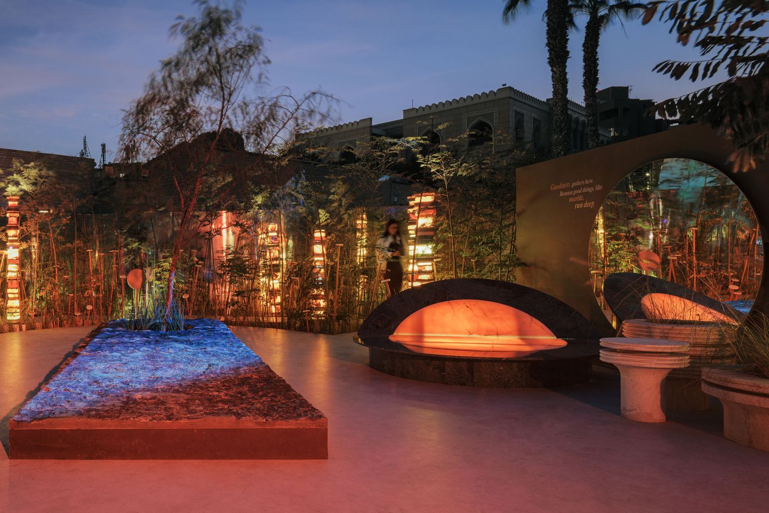 Twilight outdoor installation featuring a blue sand artwork, arched seating, and bamboo with warm lighting.