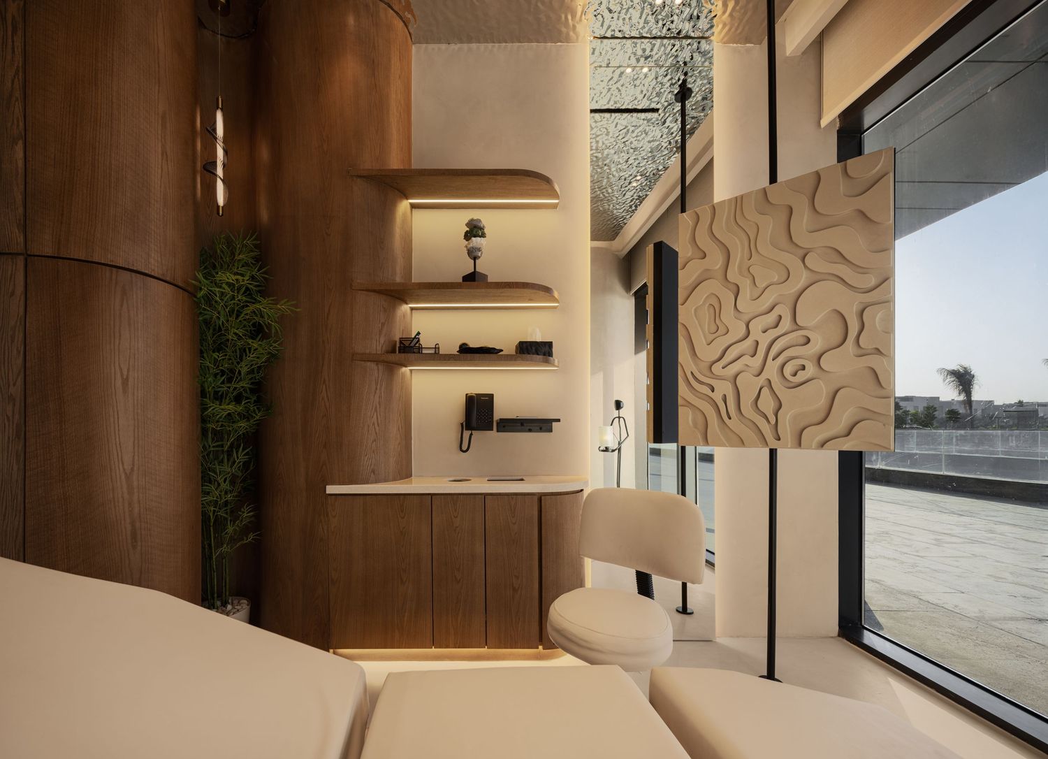 Modern luxury interior with warm wood shelving, beige chair, and decorative textured wall panel by large windows.