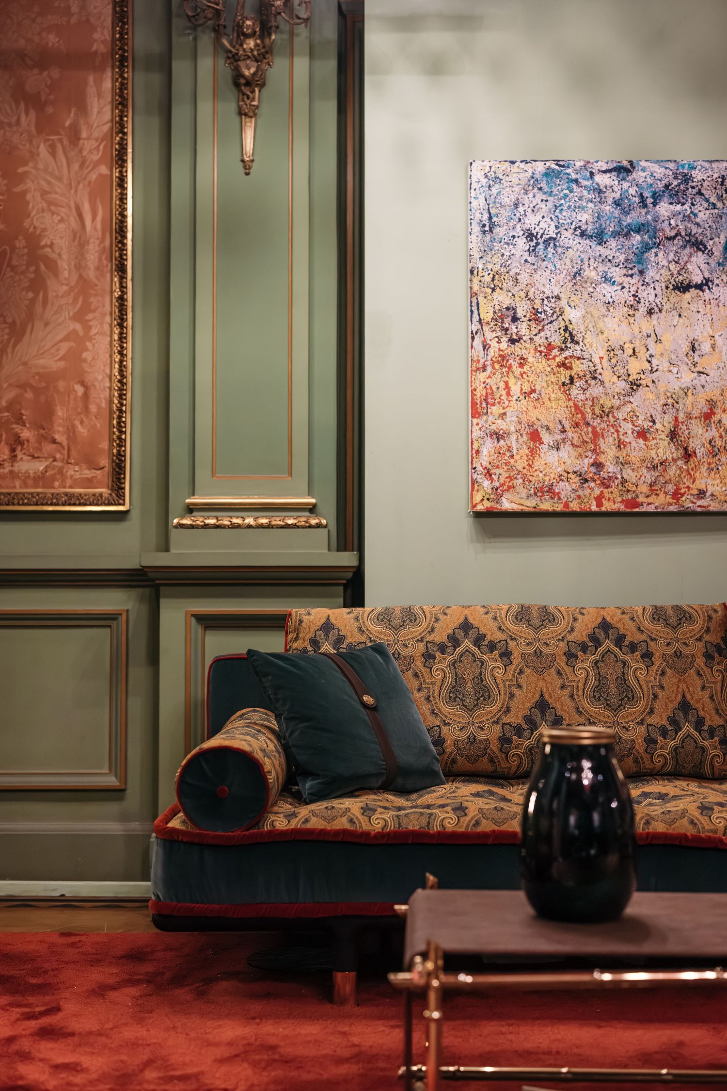 Elegant living room with patterned sofa, sage green paneling, and abstract artwork on wall.