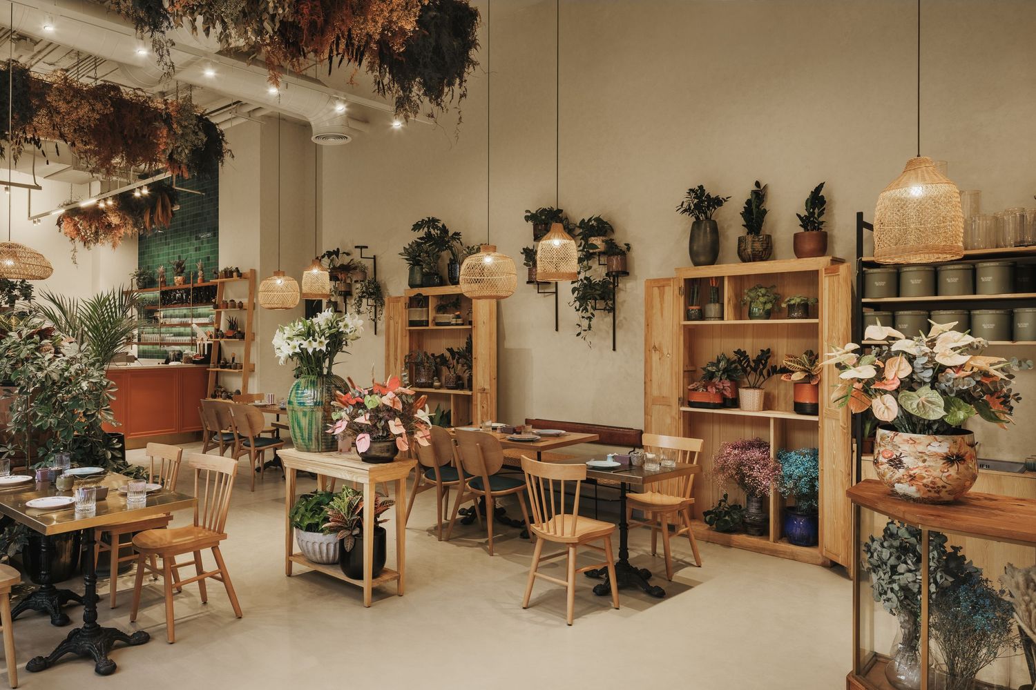 Bright botanical cafe interior with wooden furniture, hanging dried flowers, wicker pendant lights, and floral arrangements.