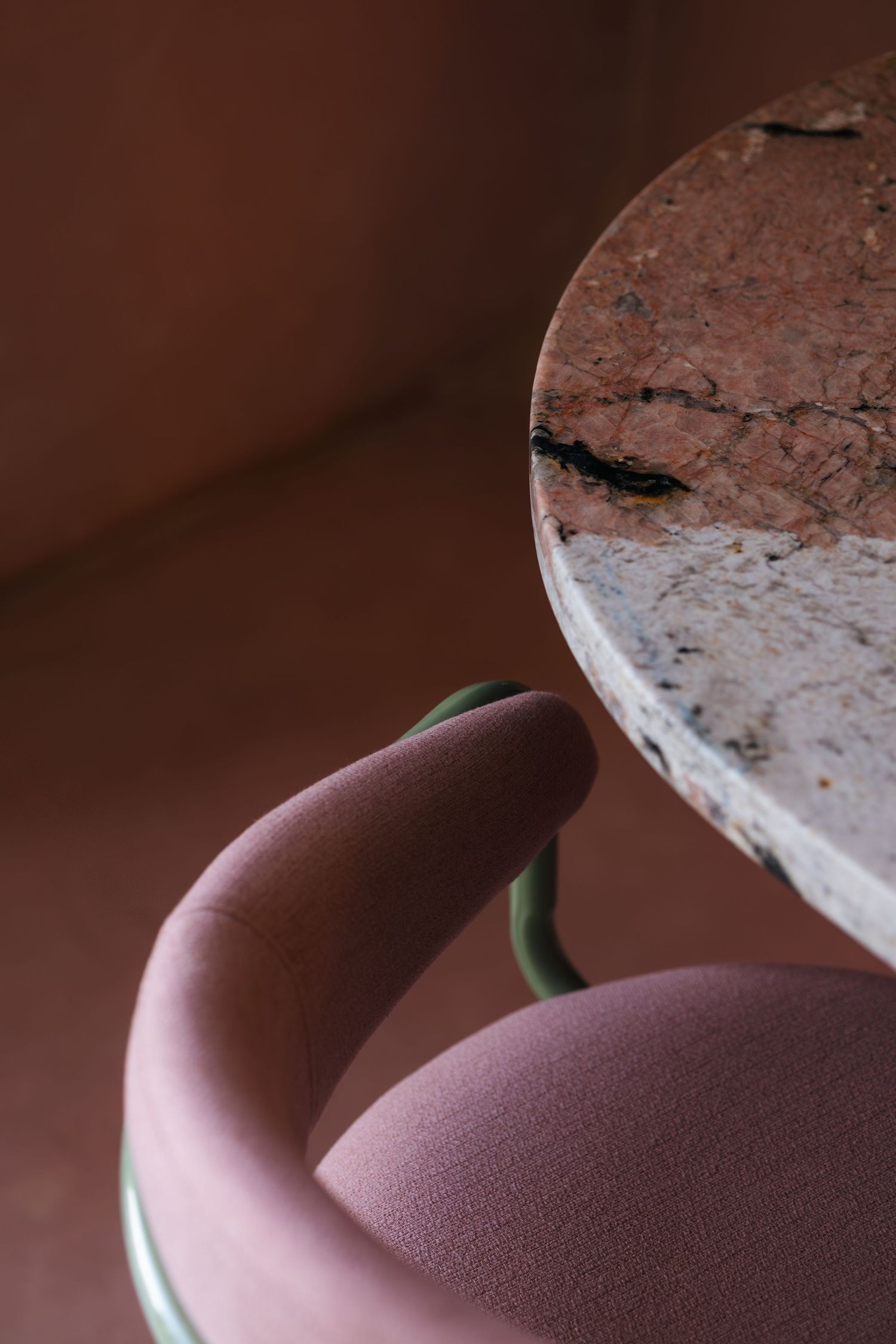 Close-up of a pink upholstered chair with green frame beside a textured marble table top.