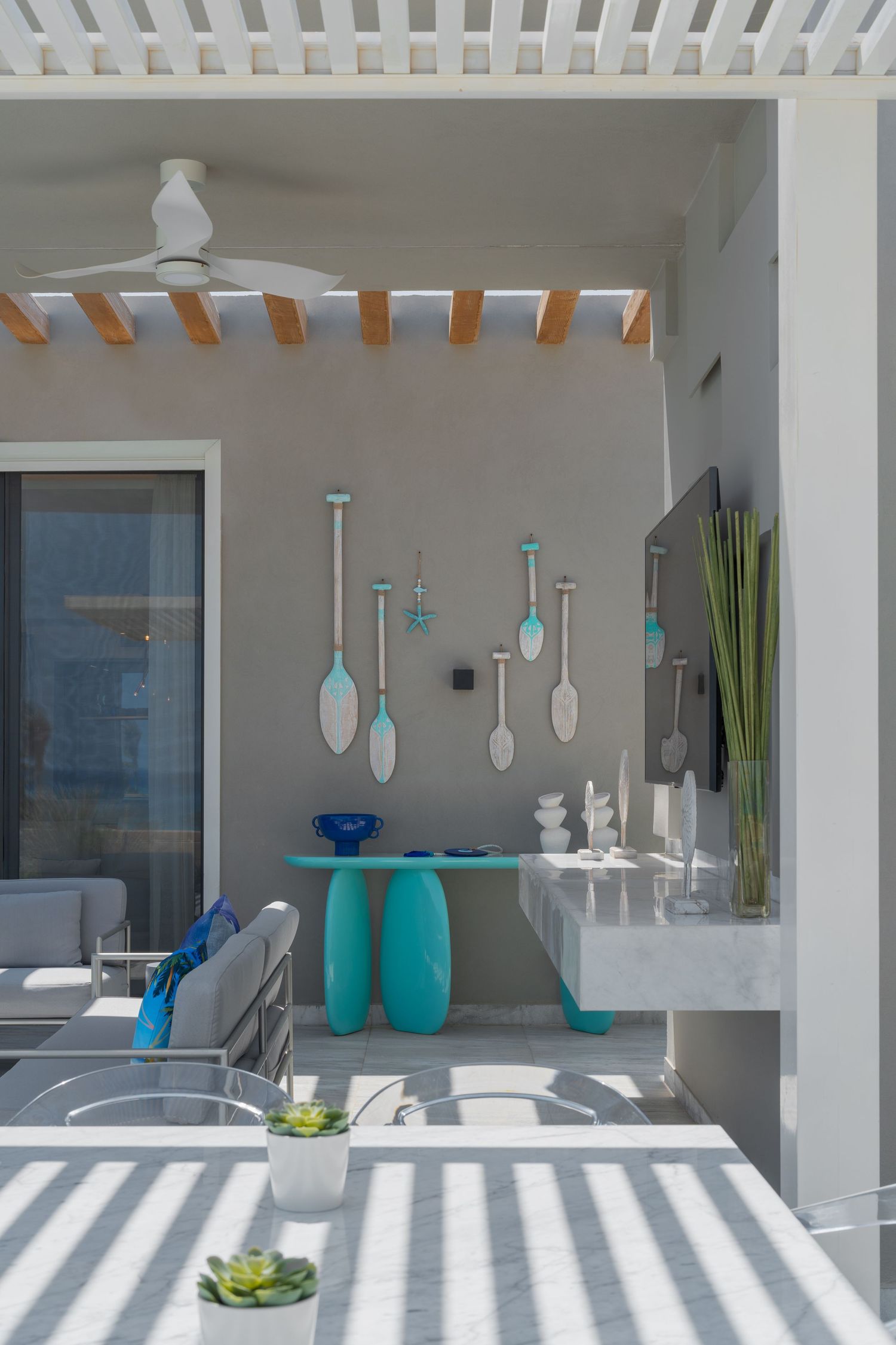 Modern outdoor patio with turquoise console table, decorative oar wall art, ceiling fan, and striped flooring.