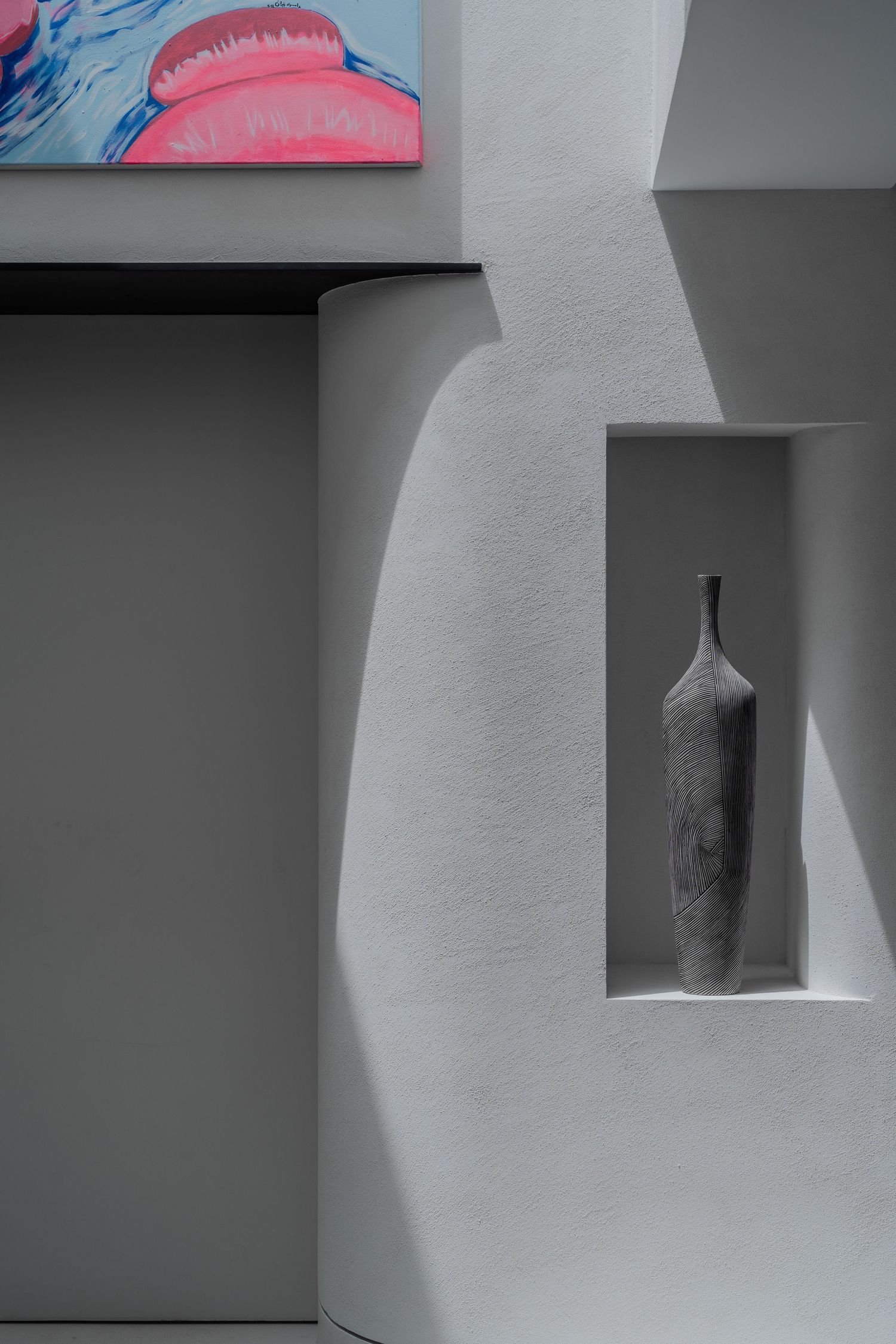 Minimalist white wall niche displaying a textured ceramic vase beside a vibrant pink abstract artwork.