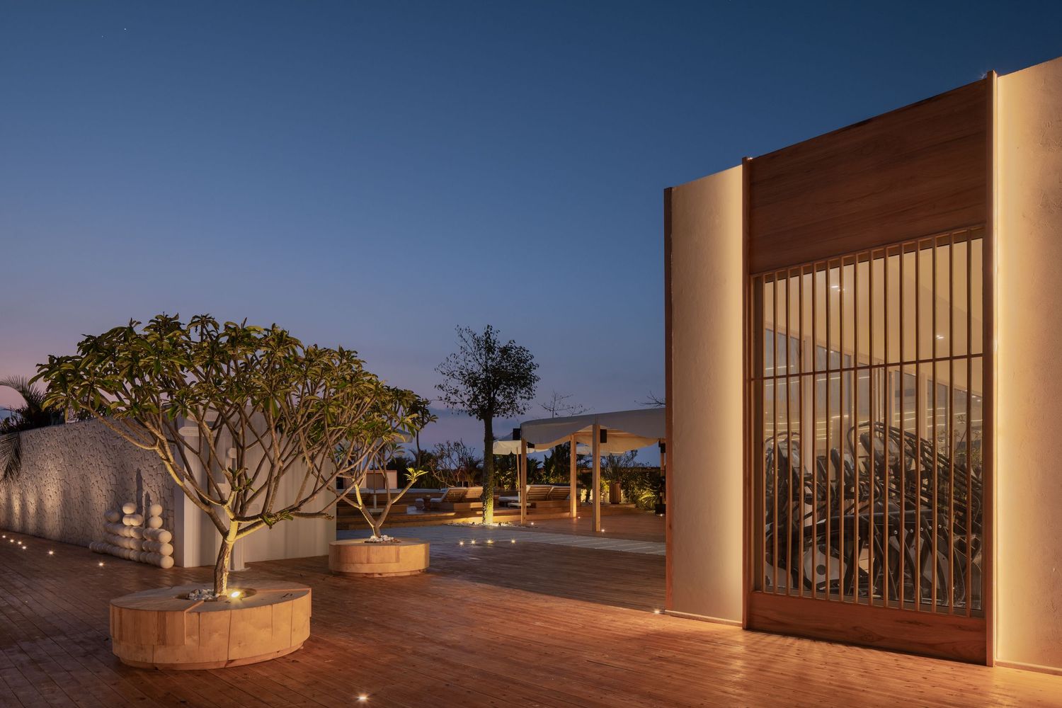 Luxury resort entrance at dusk with decorative trees in round planters, warm lighting, and ornate wooden gate details.