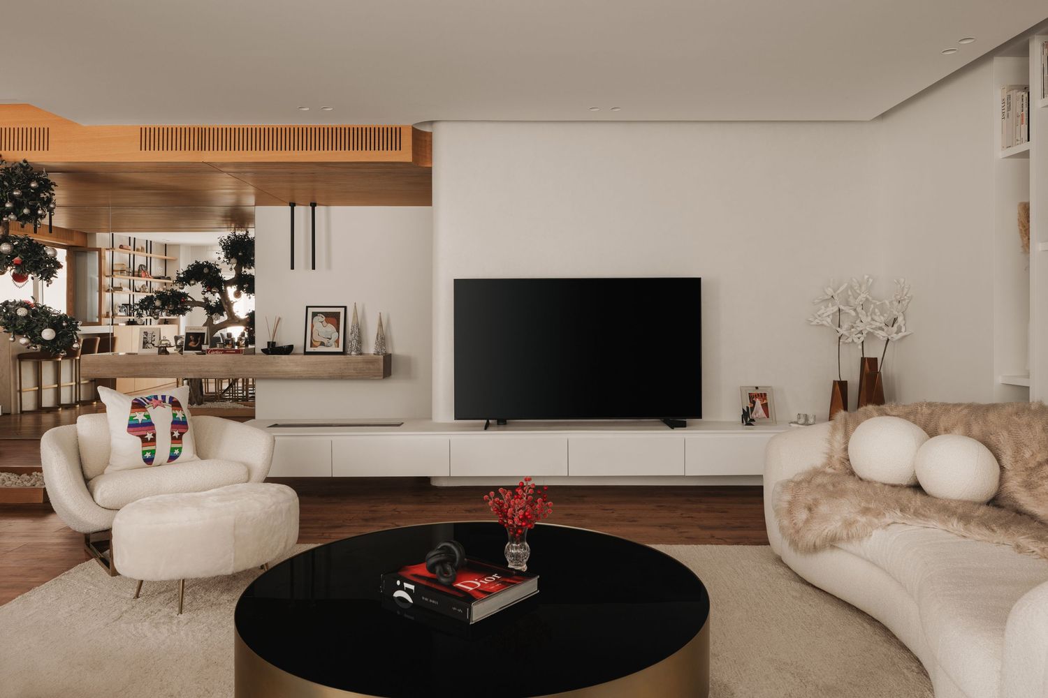 Modern living room with white bouclé sofas, black round coffee table, wall-mounted TV, and wooden ceiling accent detail.