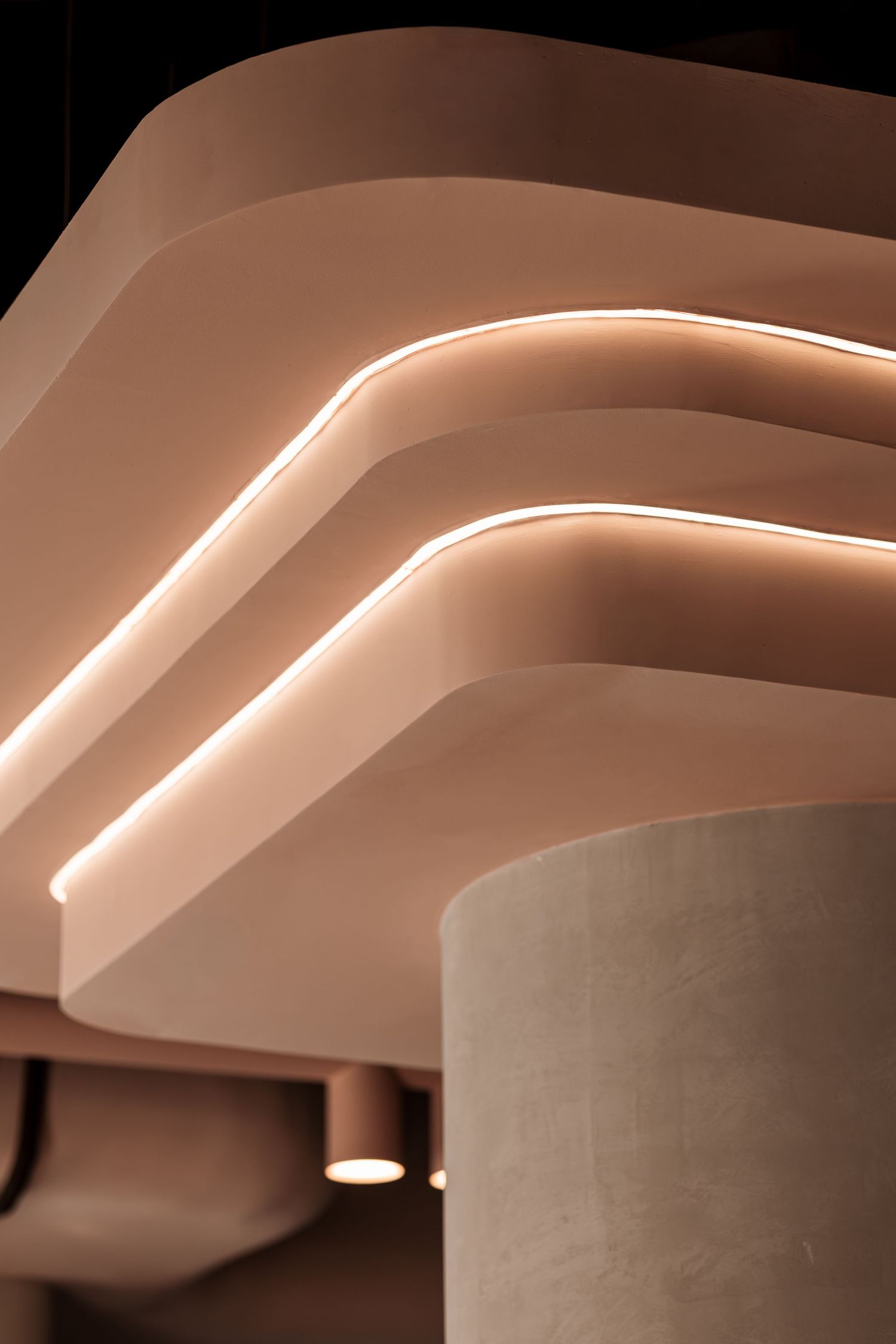 Layered curved ceiling panels with warm LED strip lighting above a cylindrical column.