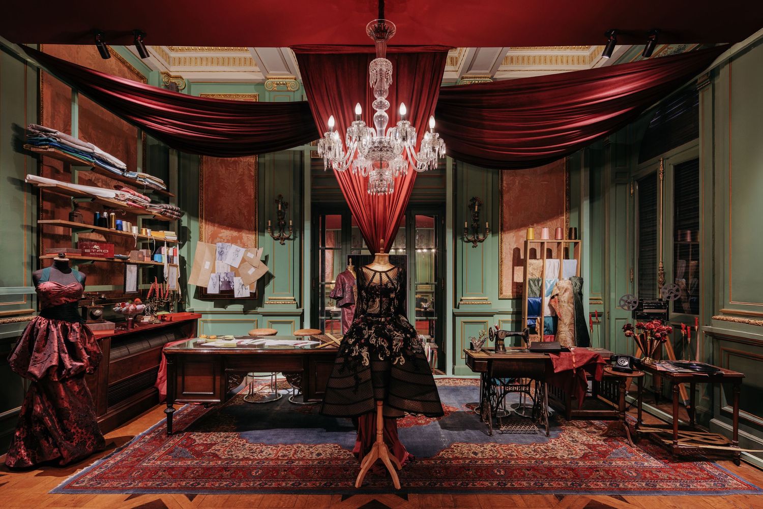 Opulent vintage atelier with red drapes, crystal chandelier, mannequin, and ornate antique sewing room decor.