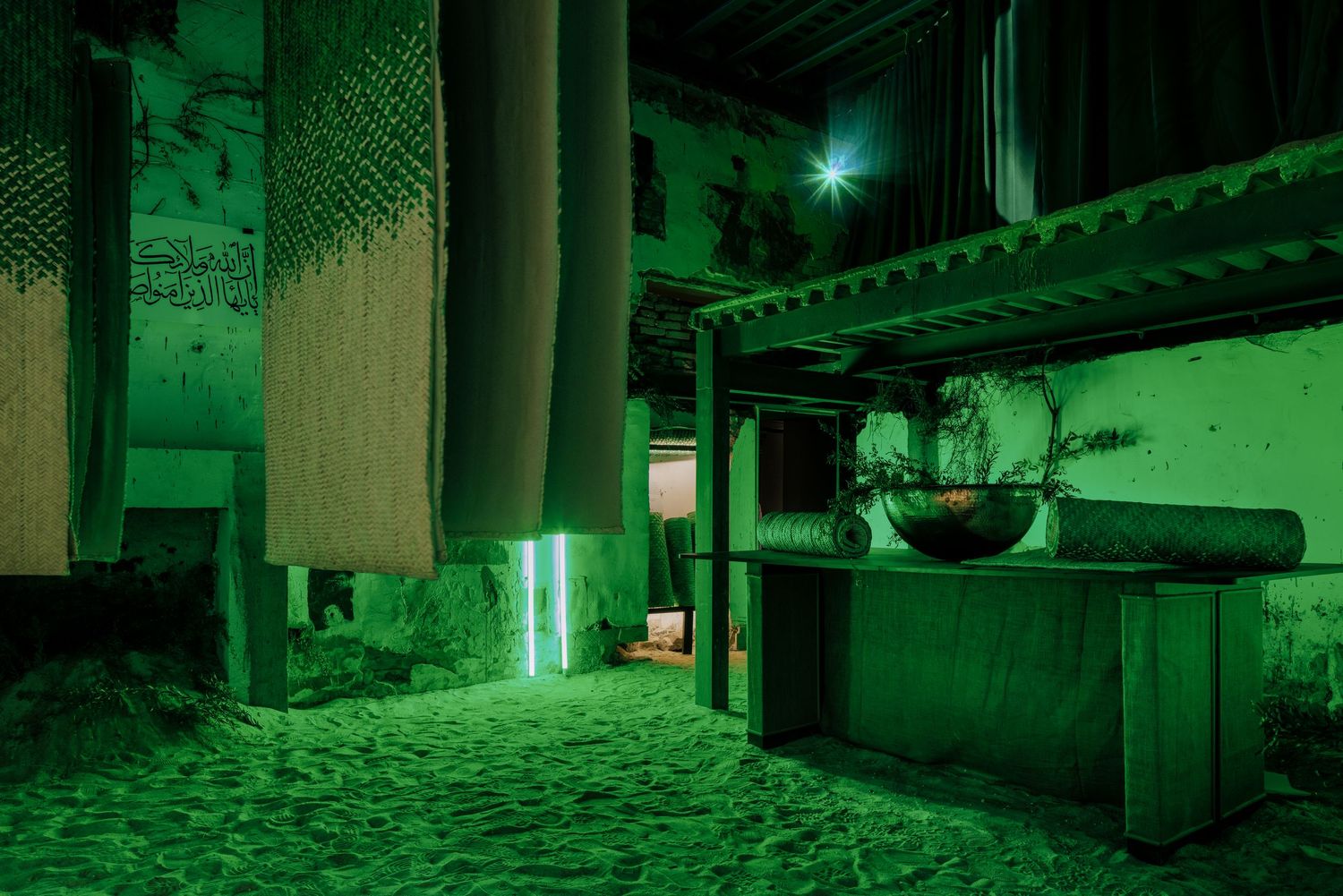 Dramatic green-lit underground space with hanging textiles, rustic wooden furniture, and a glowing star overhead.