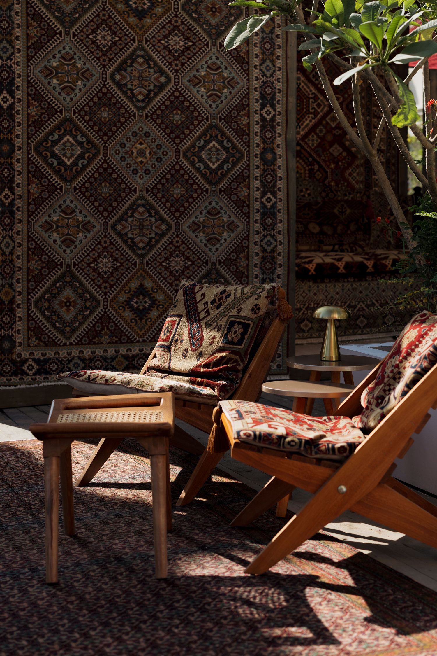 Two wooden lounge chairs with patterned cushions on a rug with a large decorative carpet backdrop.