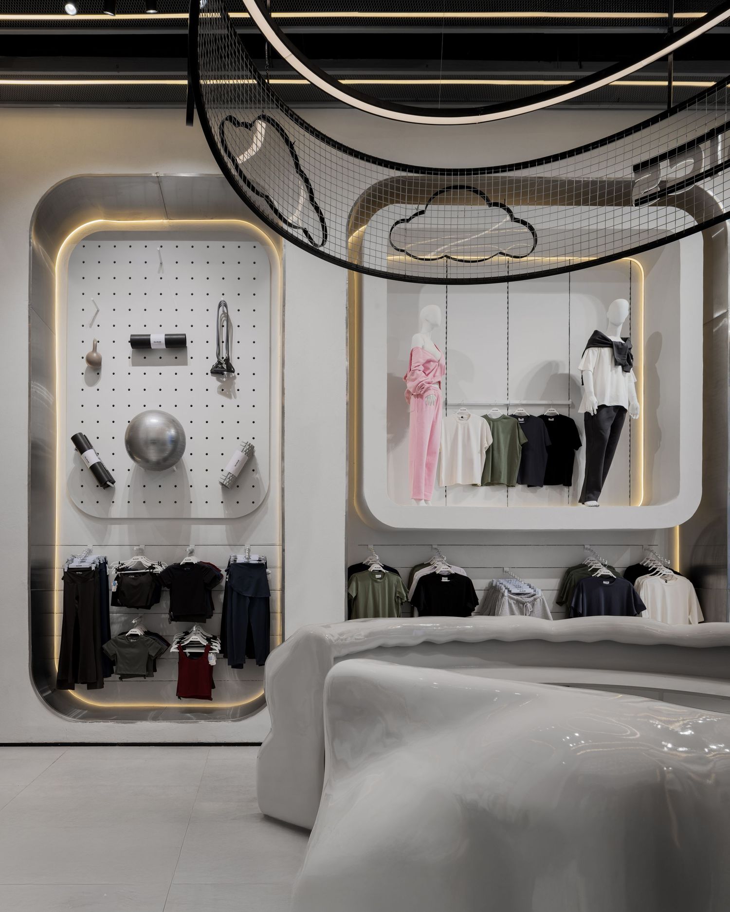 Futuristic white retail store with rounded display niches, pegboard accessories wall, hanging clothes, and overhead net installation.