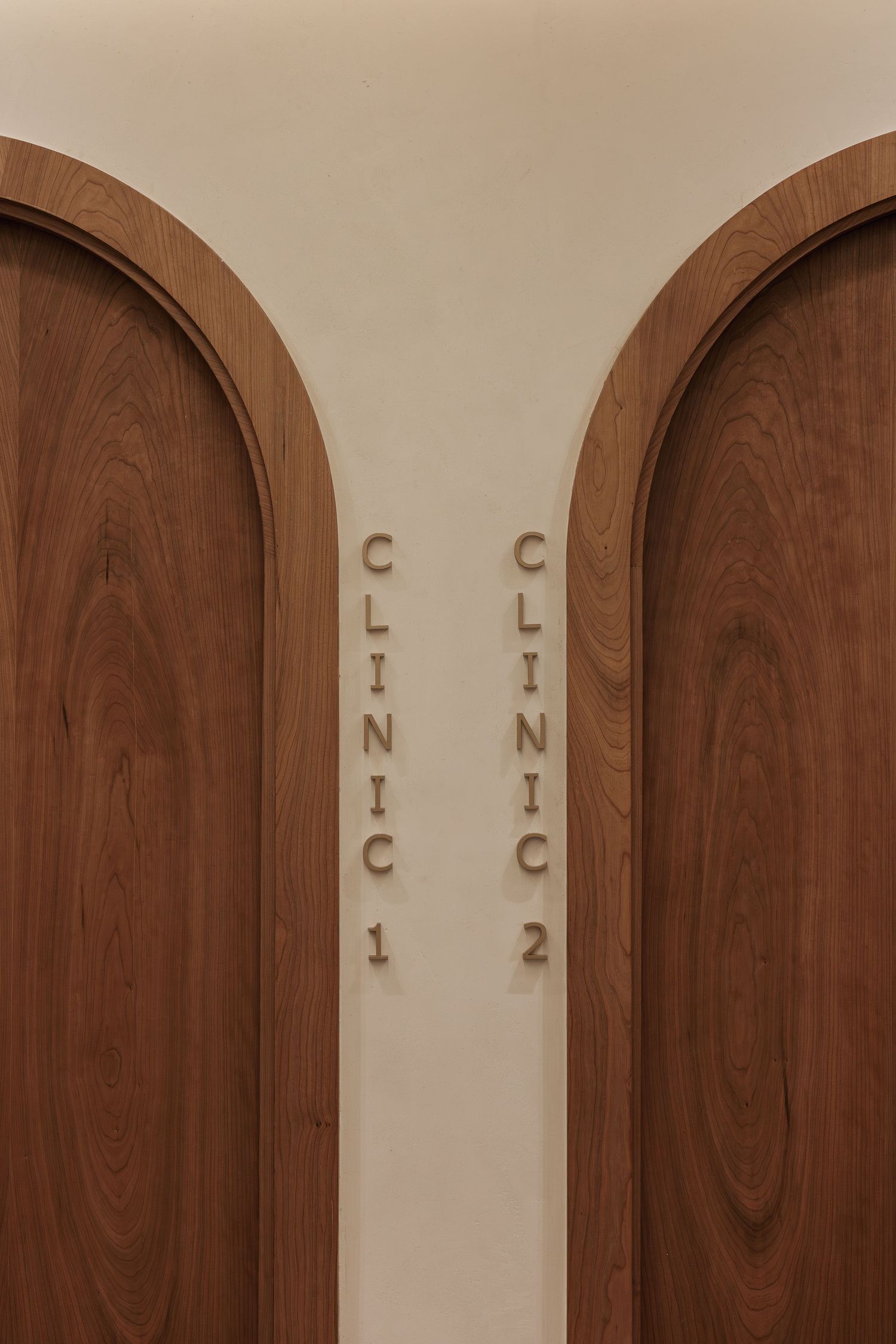 Two arched walnut wood clinic doors with raised letter signage reading Clinic 1 and Clinic 2.