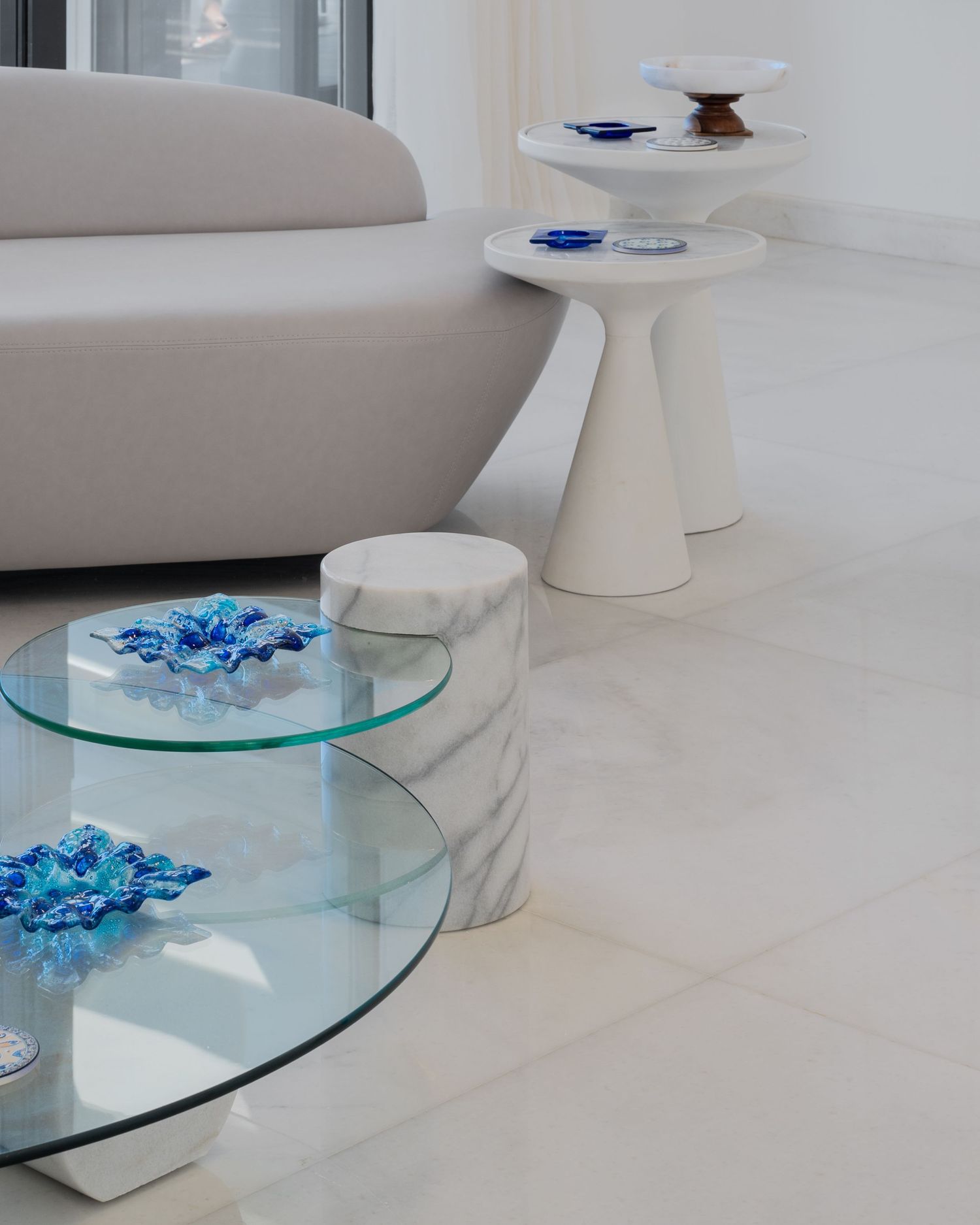 White marble coffee table with glass top and blue floral decor beside a white sofa on polished tile floor.