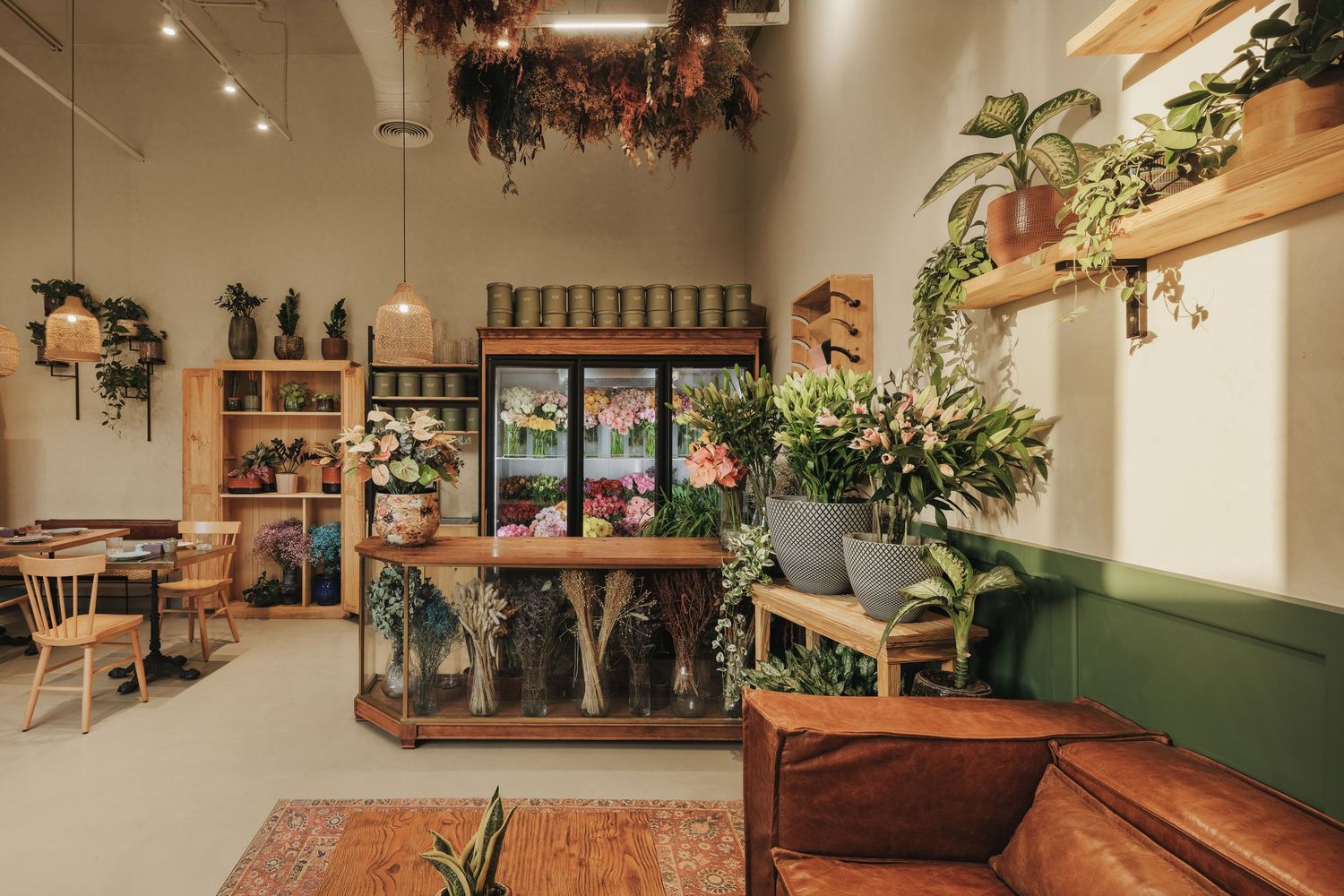 Charming flower shop interior with leather sofa, floral display fridge, and lush hanging plants.