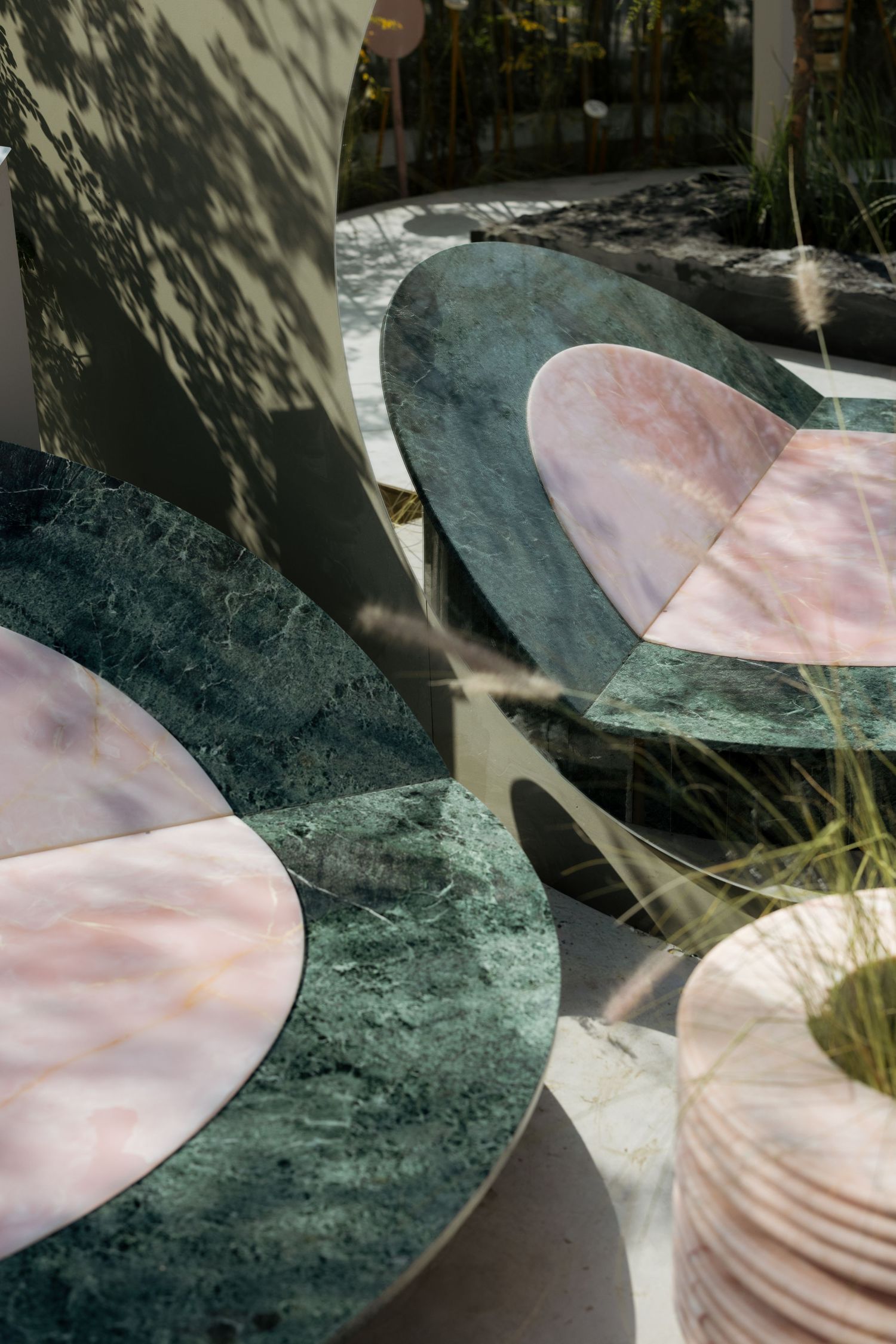 Green and pink marble circular table tops with overlapping geometric designs in a sunlit garden setting.