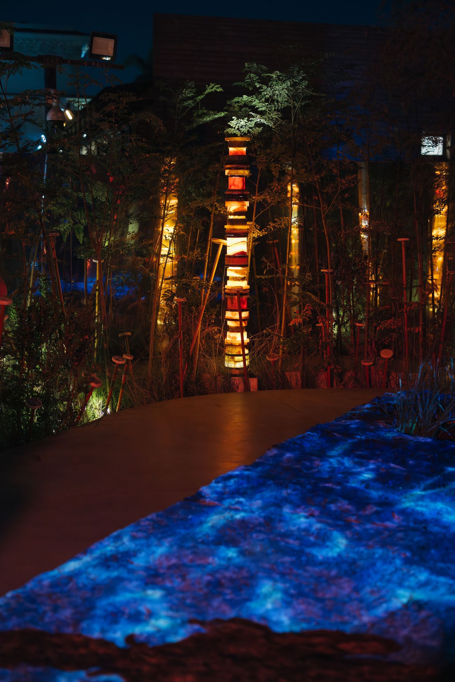 Illuminated tower of stacked stone discs glowing amber among bamboo stalks in a nighttime garden installation.