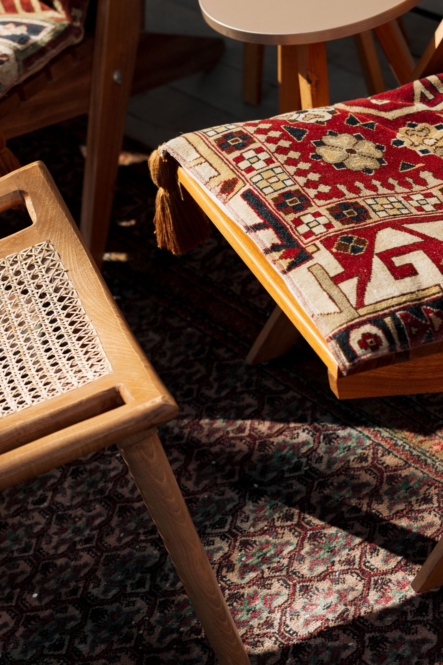 Close-up of a colorful traditional kilim rug draped over a wooden chair with woven cane seat in sunlight.