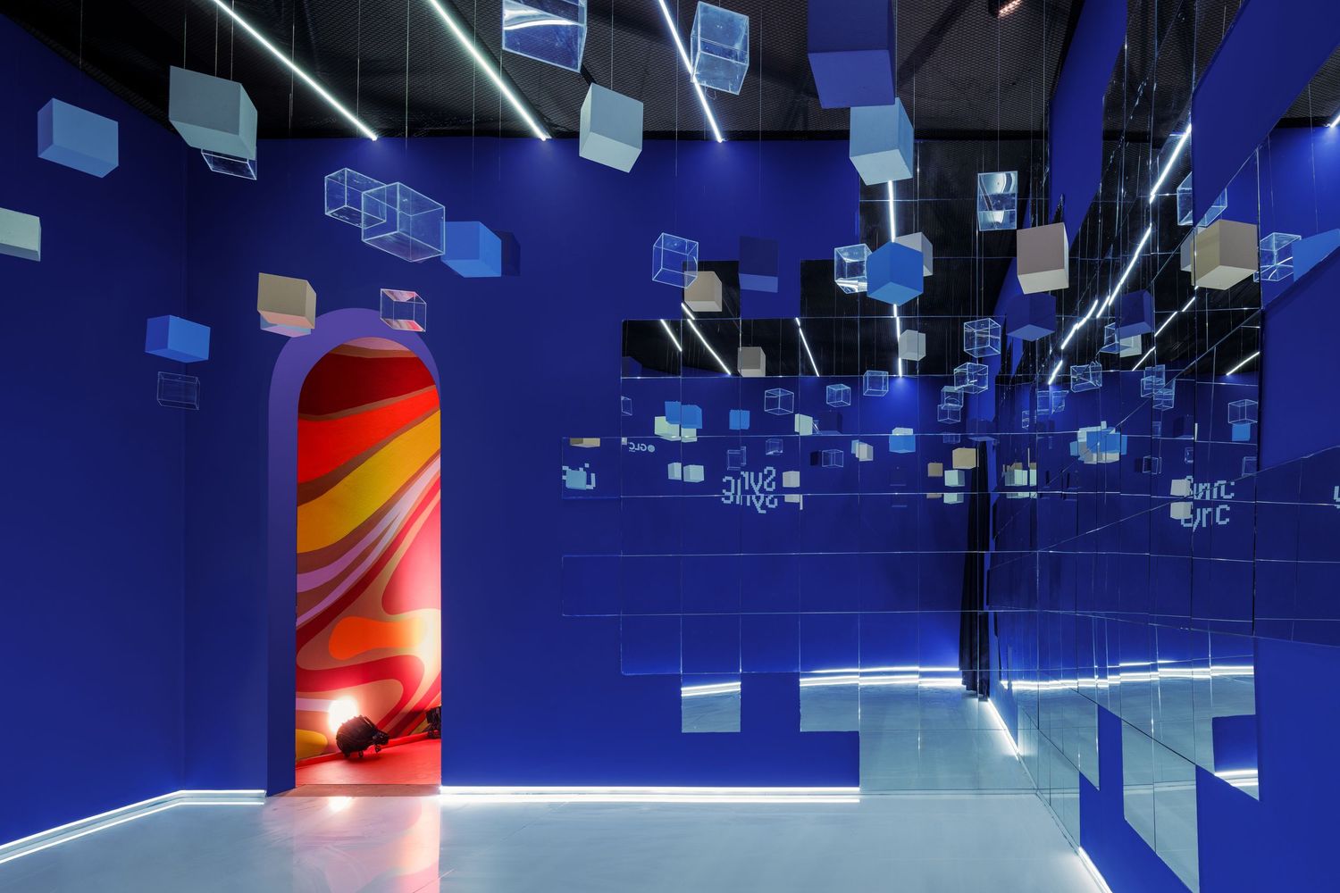 Vibrant blue mirrored gallery space with suspended cubes and colorful swirling arched doorway installation.