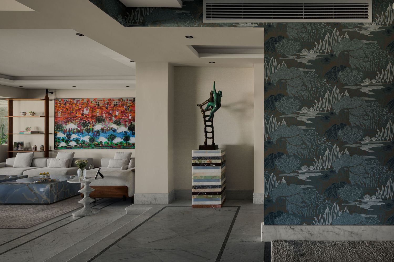 Open plan living space with colorful artwork, bronze ladder sculpture, botanical wallpaper, and gray sectional sofa.