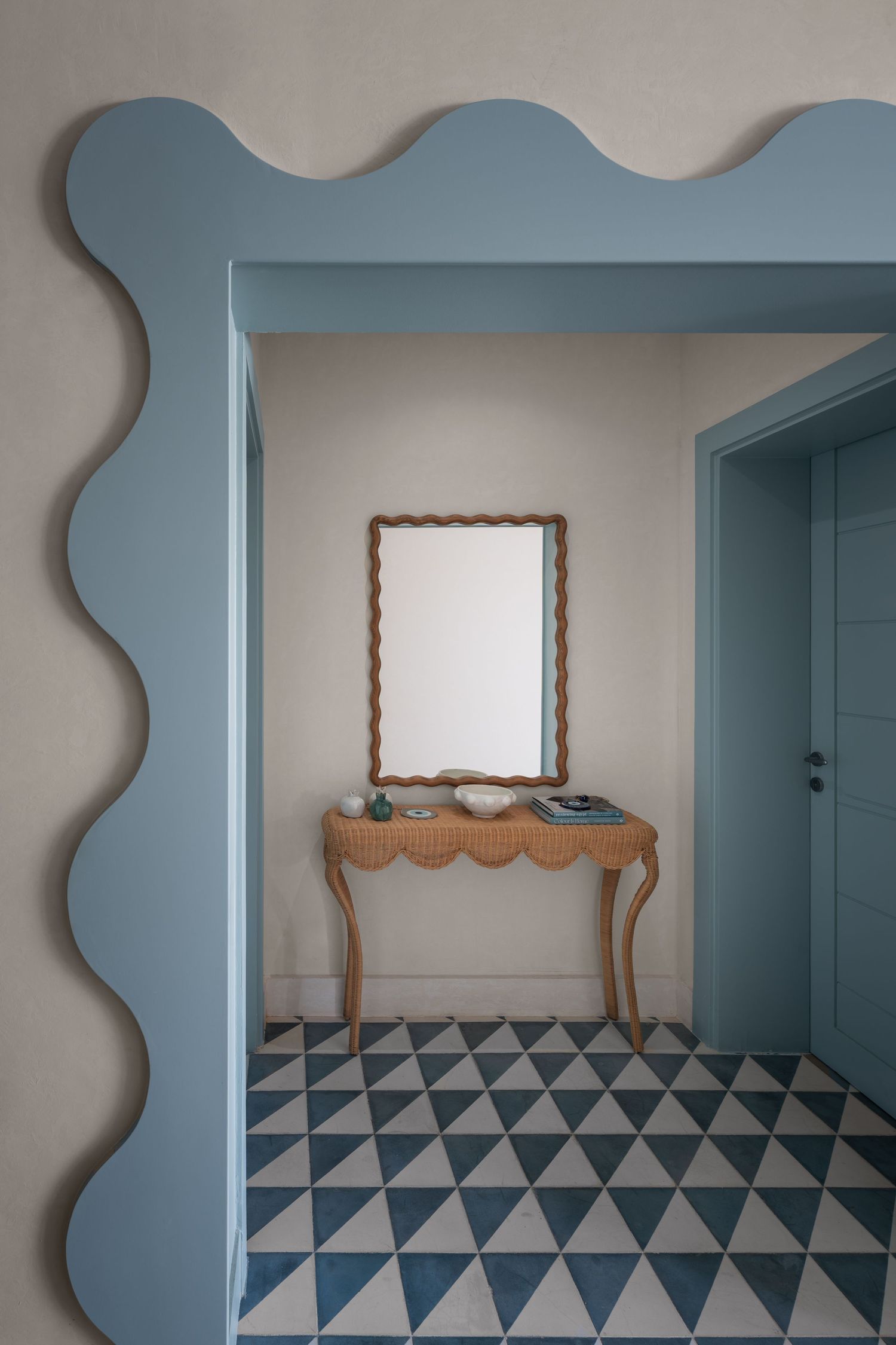 Elegant entryway with wavy blue doorframe, geometric tile floor, wooden console table and decorative mirror.