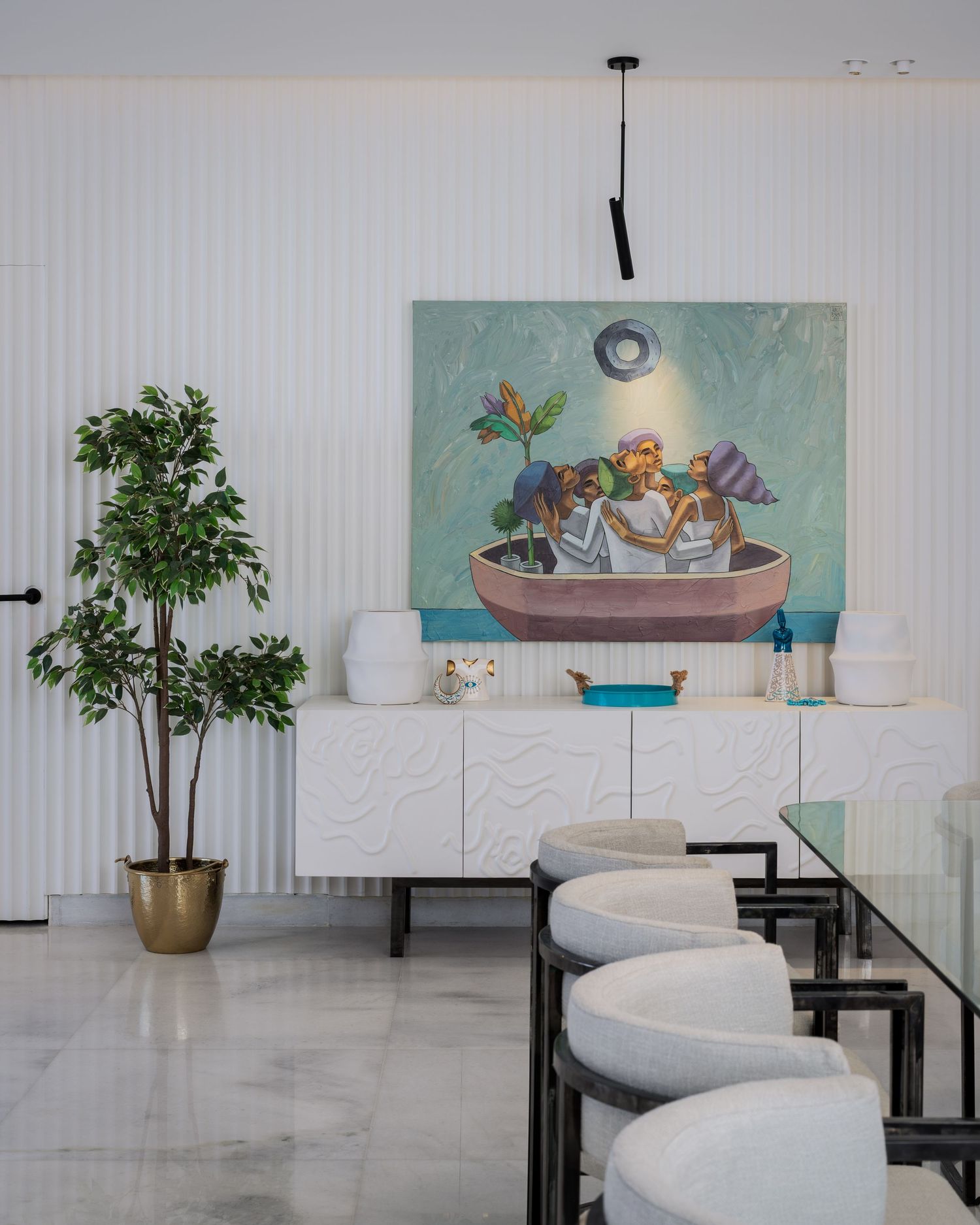Contemporary dining area with white textured sideboard, large teal still-life painting, potted tree, and gray bar stools.