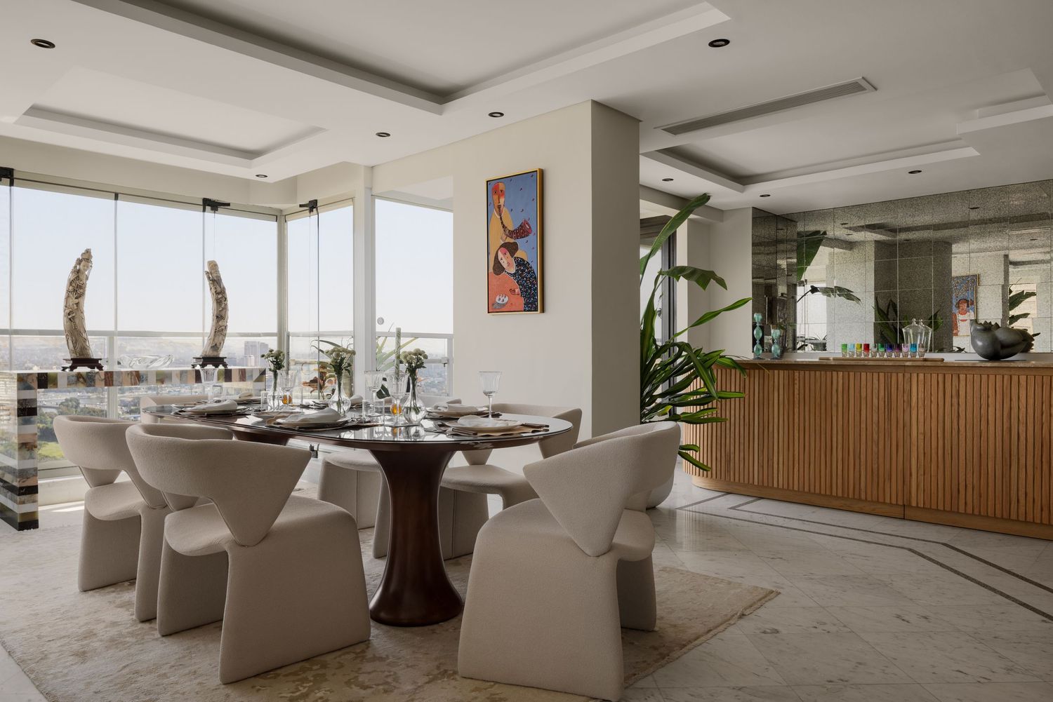 Elegant dining room with round glass table, cream chairs, floor-to-ceiling windows, and colorful wall art in luxury apartment.