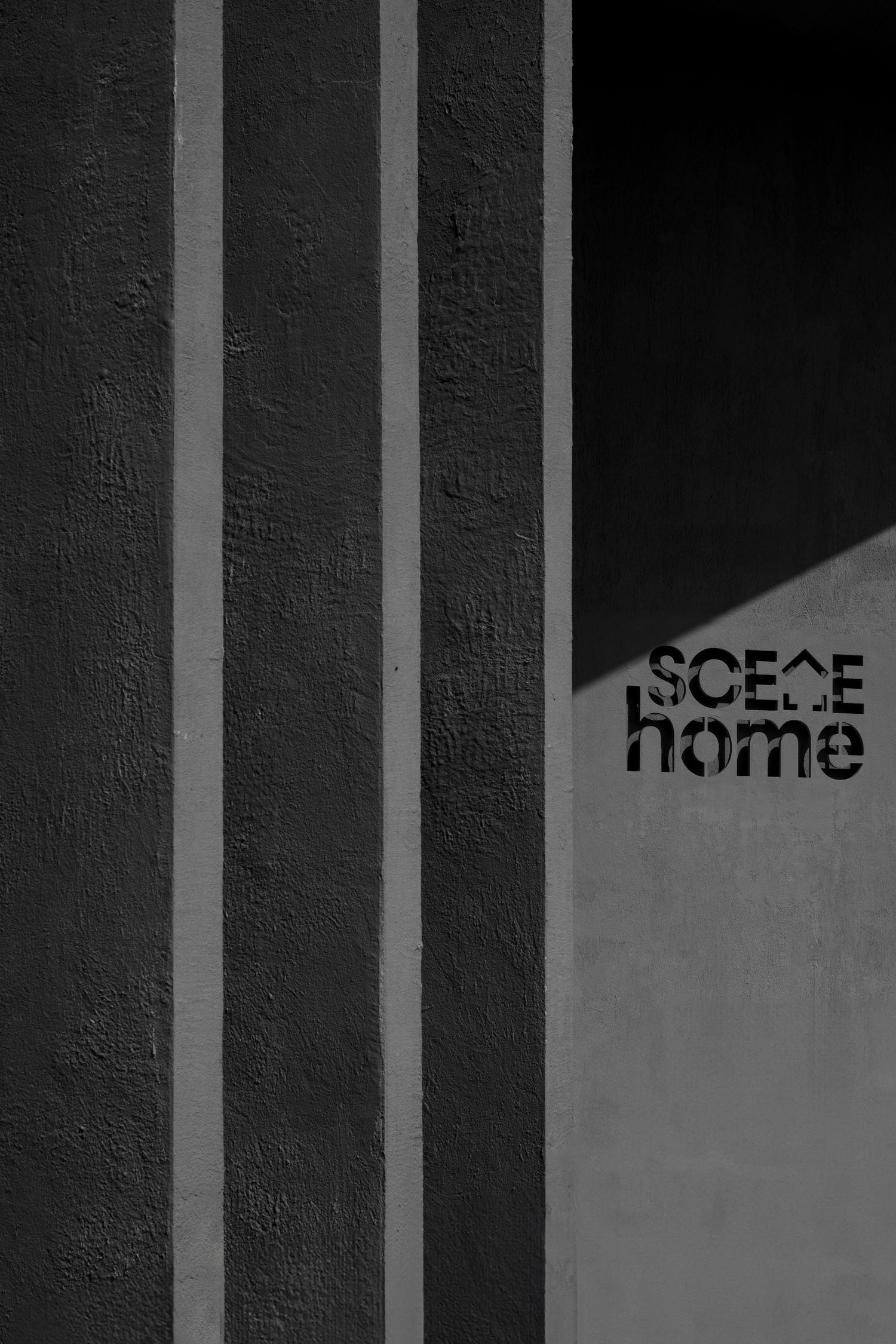 Black and white photo of textured concrete wall with vertical ridges and SCENE home signage.