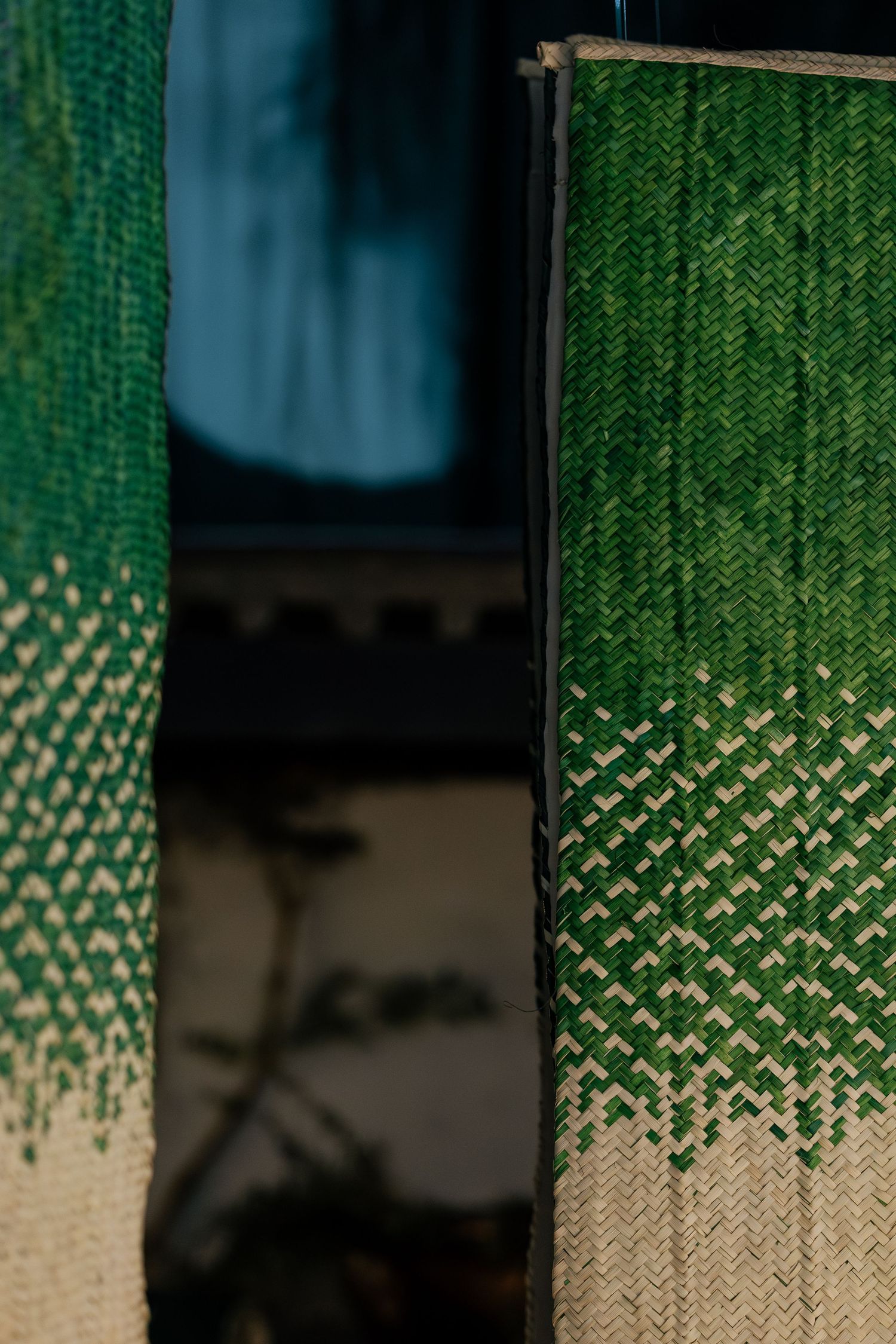 Close-up of green and beige woven textile panels with herringbone pattern hanging beside a dark mirror.