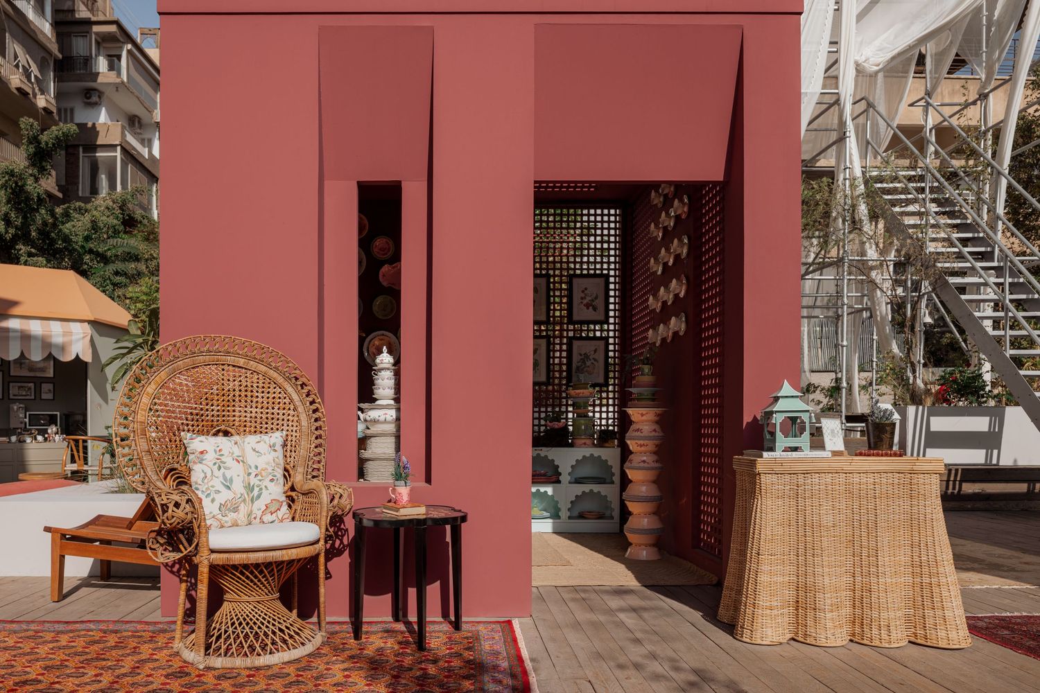 Terracotta pink pavilion with rattan furniture and decorative lattice screens outdoors.