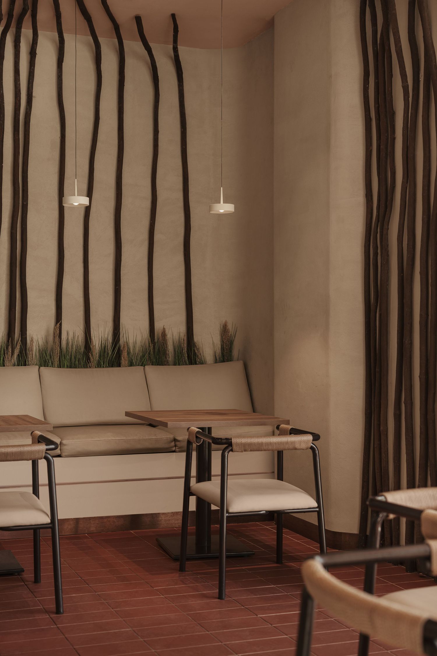 Intimate restaurant booth with organic branch wall art, beige upholstered seating, wooden tables, and pendant lighting.