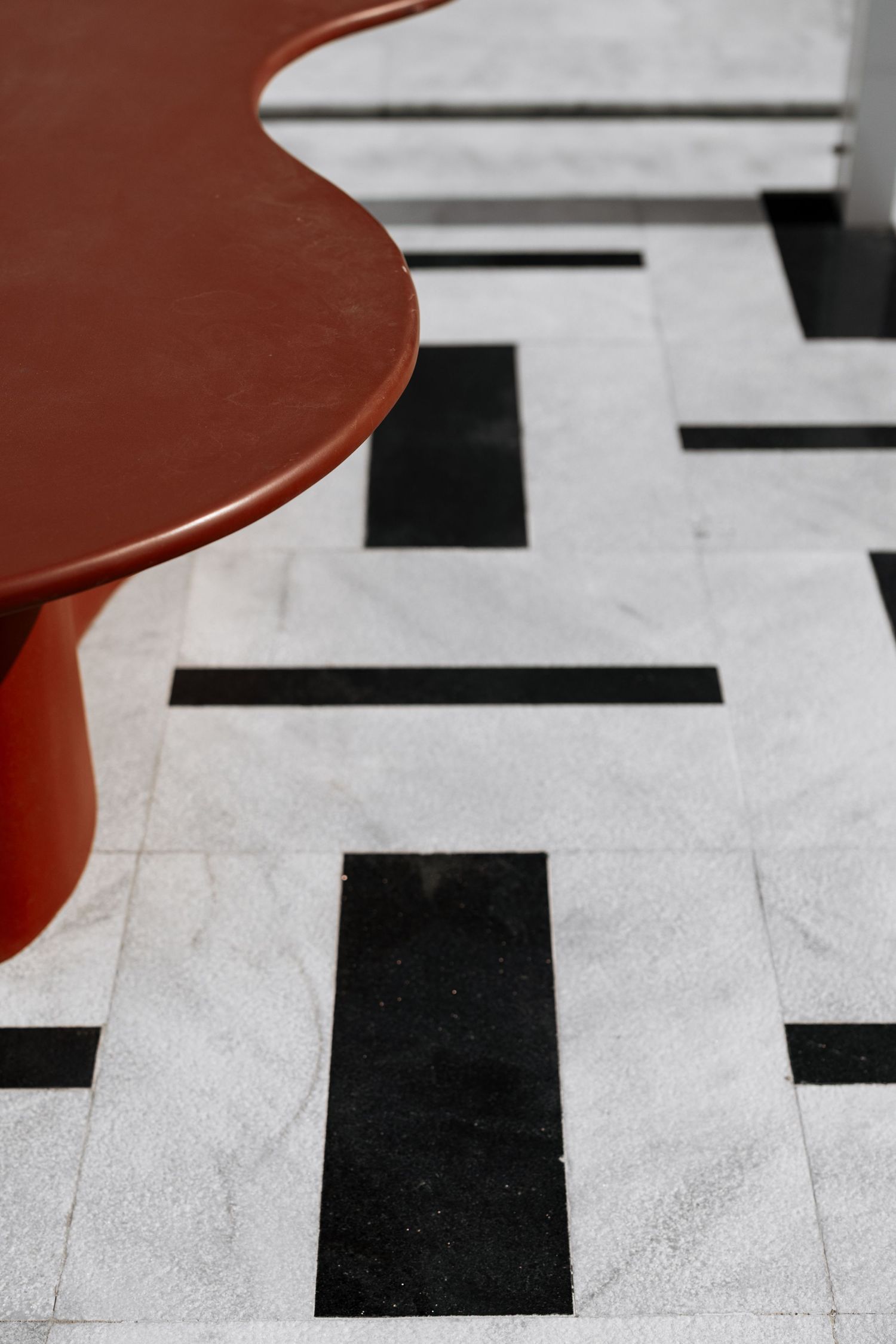 Red table on black and white geometric marble floor tiles in modern interior design.