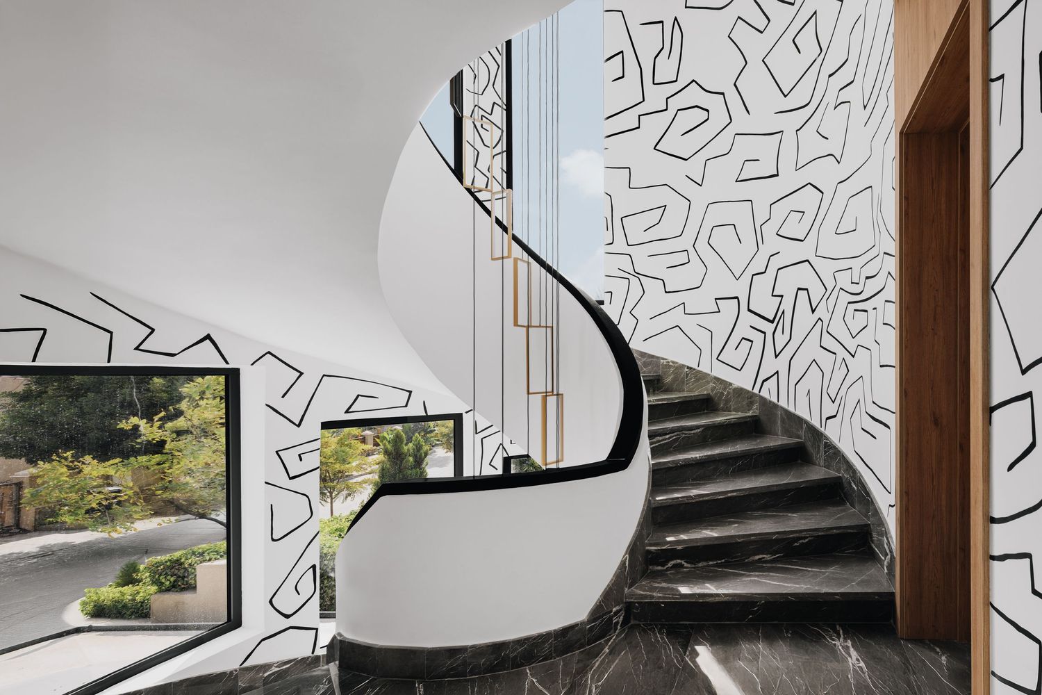 Elegant curved staircase with dark marble steps, gold handrail accents, and bold black and white abstract patterned feature wall.