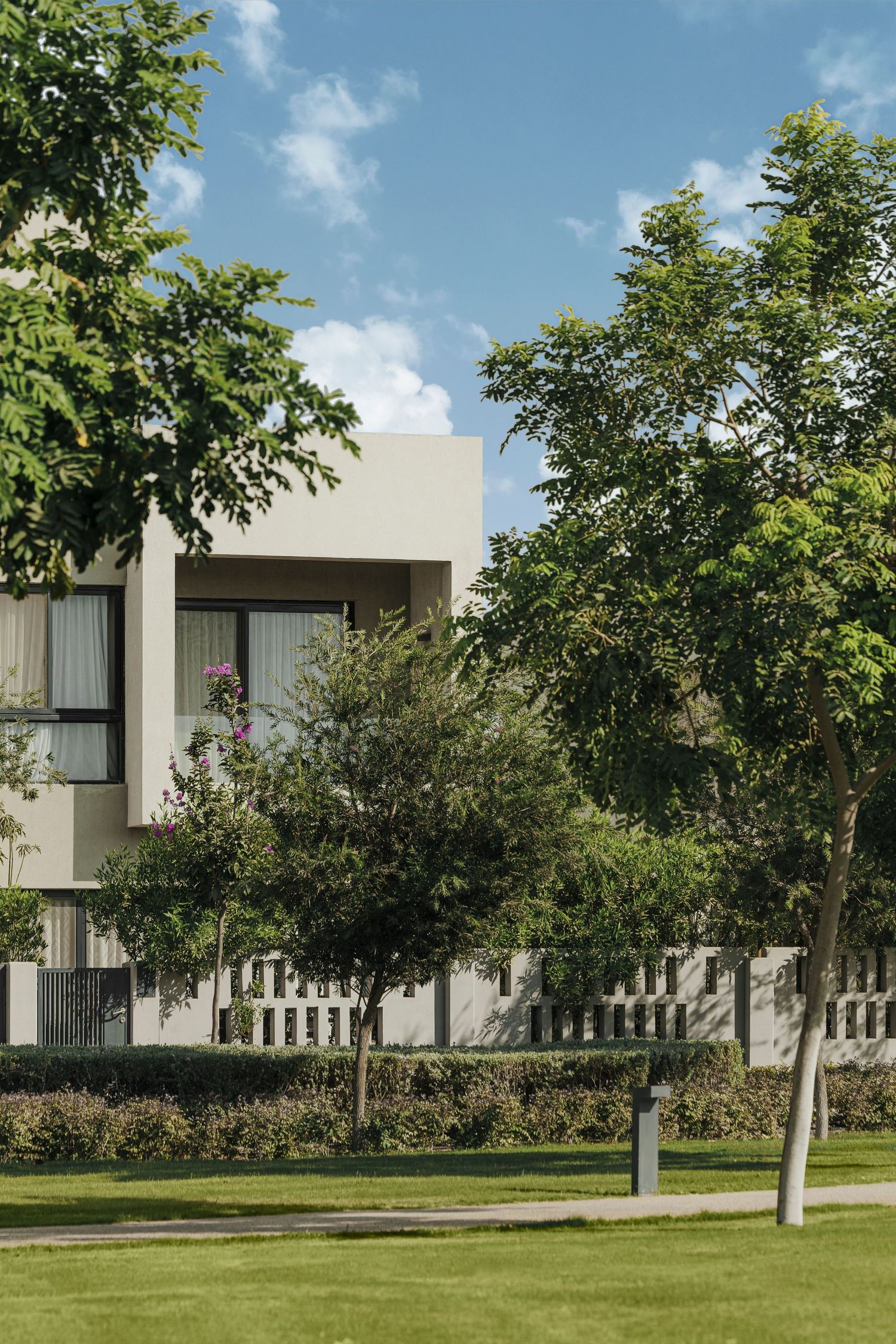 Contemporary white residential building surrounded by mature green trees and manicured lawn under a bright blue sky.
