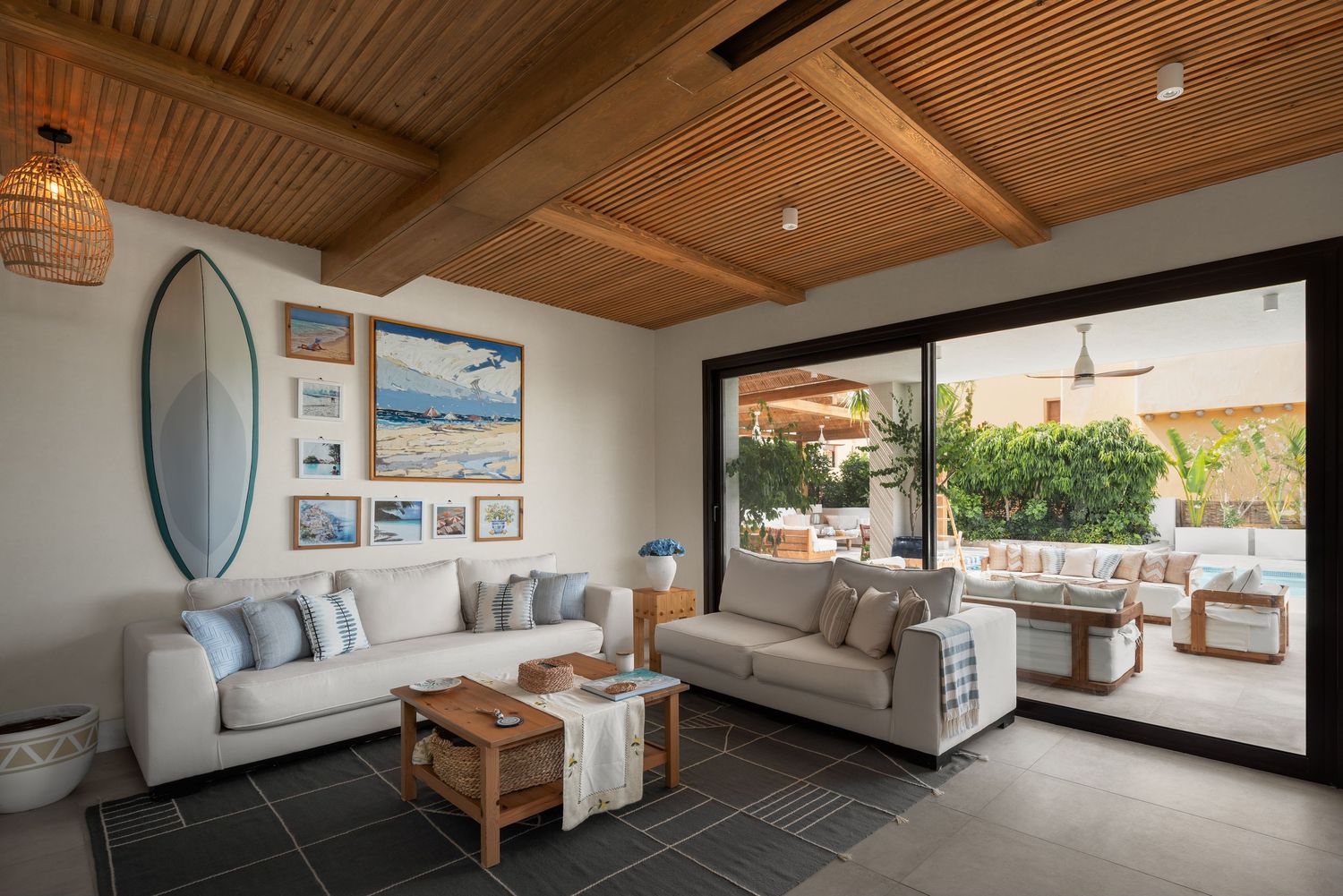 Bright coastal living room with white sofas, surfboard wall art and sliding doors to pool terrace.
