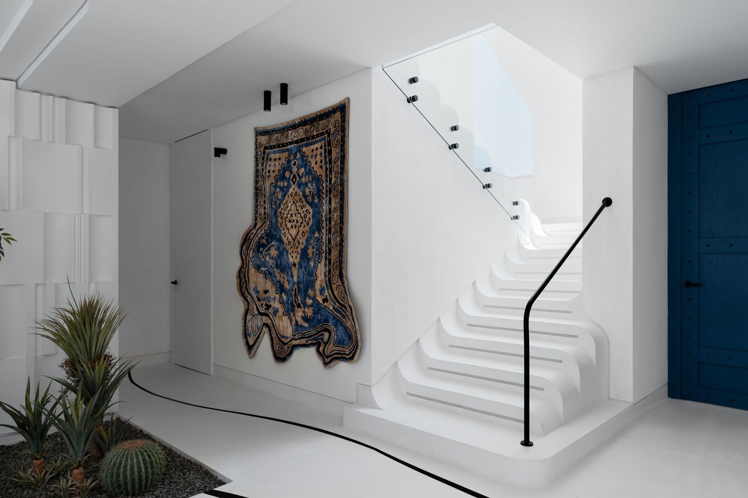 White minimalist staircase with ornate blue and gold tapestry wall art and tropical cactus garden below.