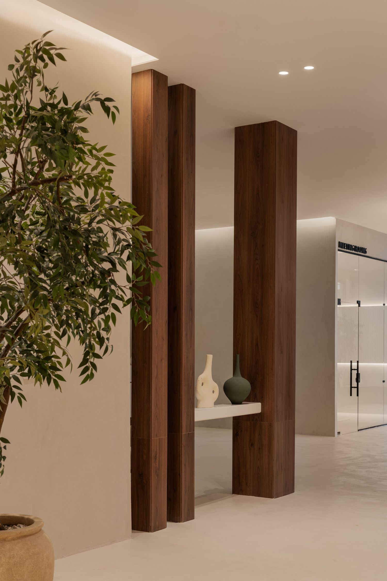 Modern interior with tall dark walnut columns, decorative vases on shelf, lush green tree, and soft recessed lighting.
