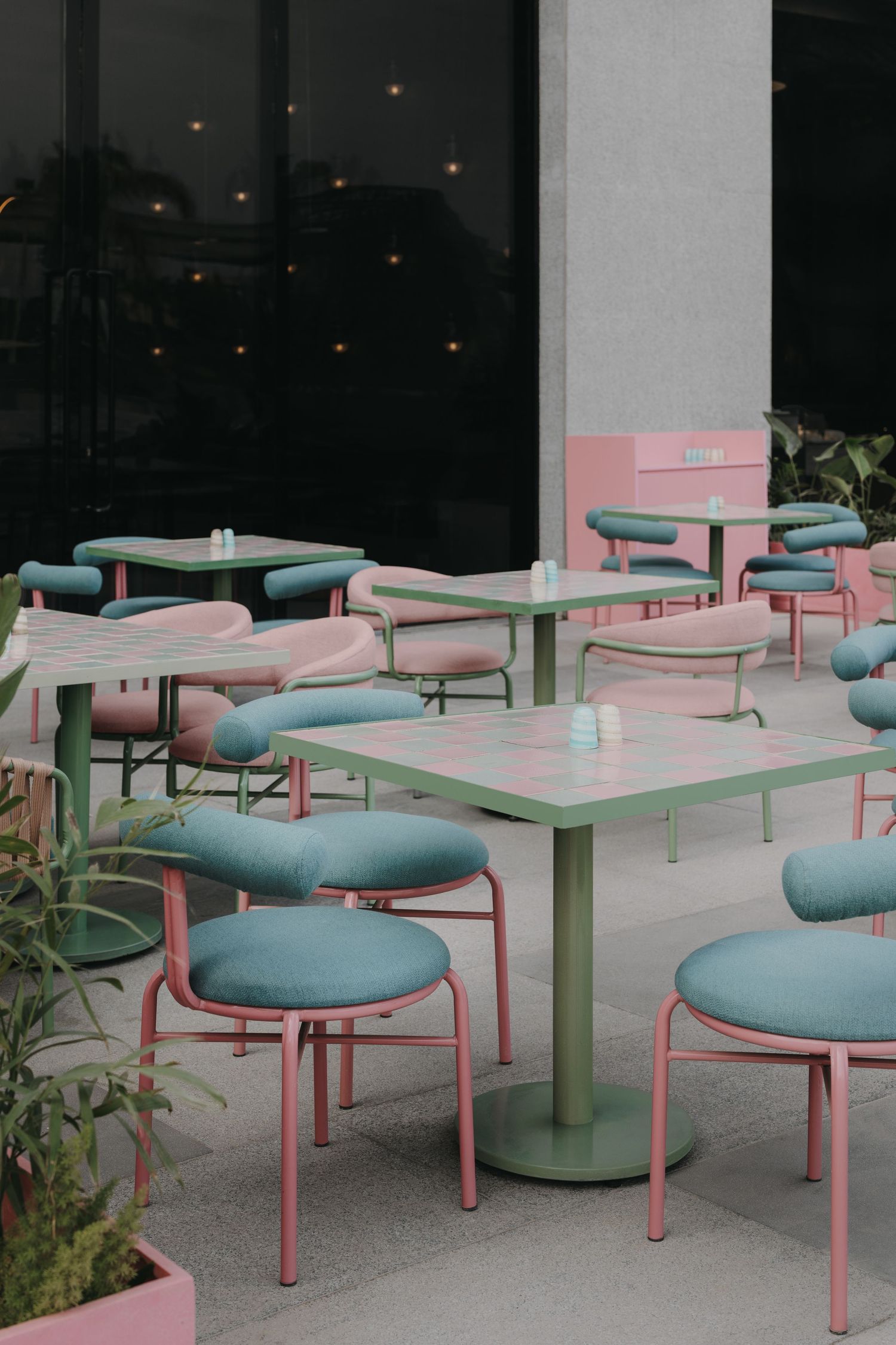 Pastel pink and teal outdoor cafe seating with green metal tables on a patio.