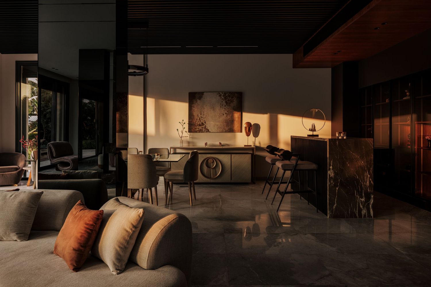 Moody evening interior with warm ambient lighting highlighting a dining area, marble bar, and neutral furnishings.