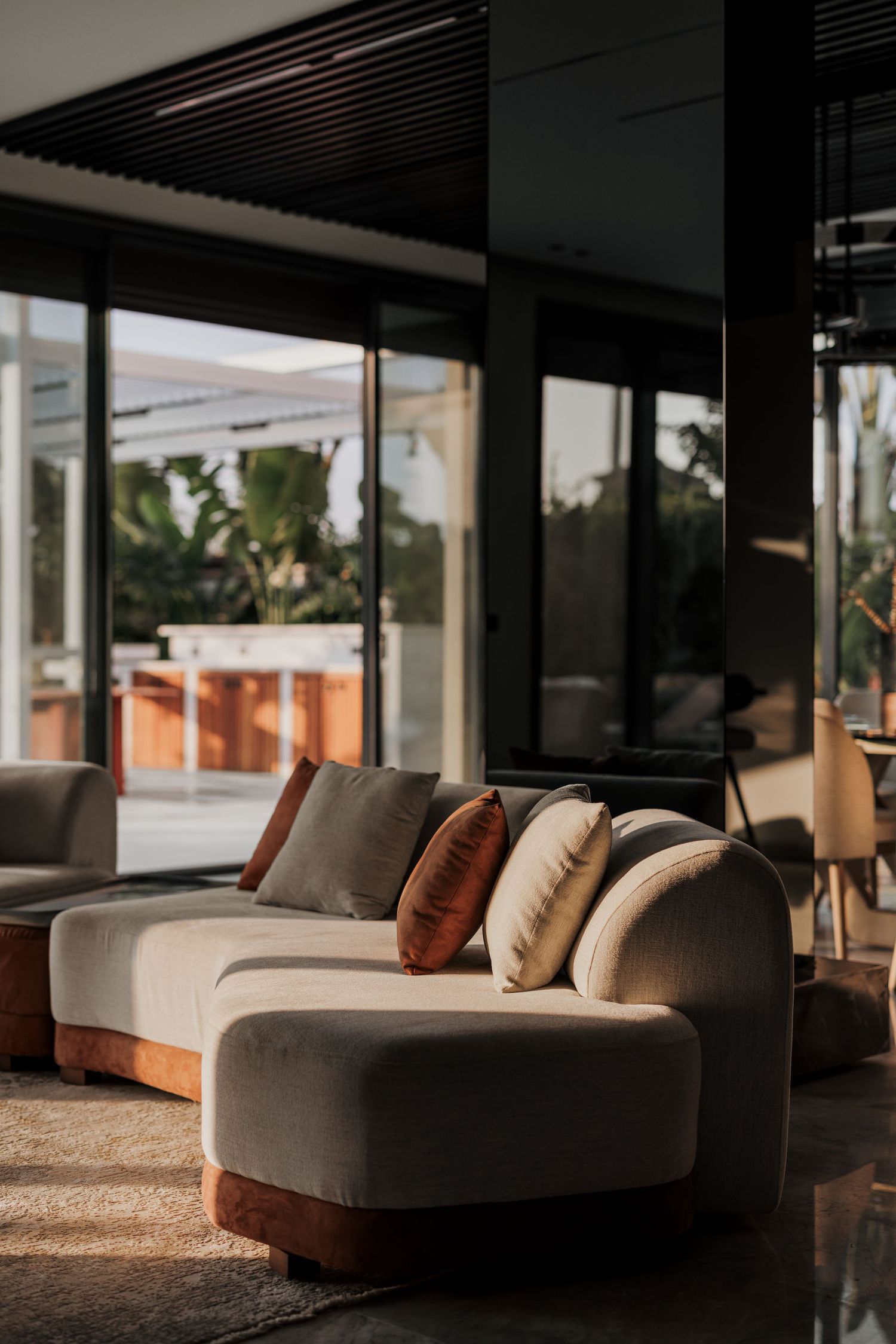Close-up of a curved beige velvet sofa with warm-toned cushions bathed in golden natural sunlight.