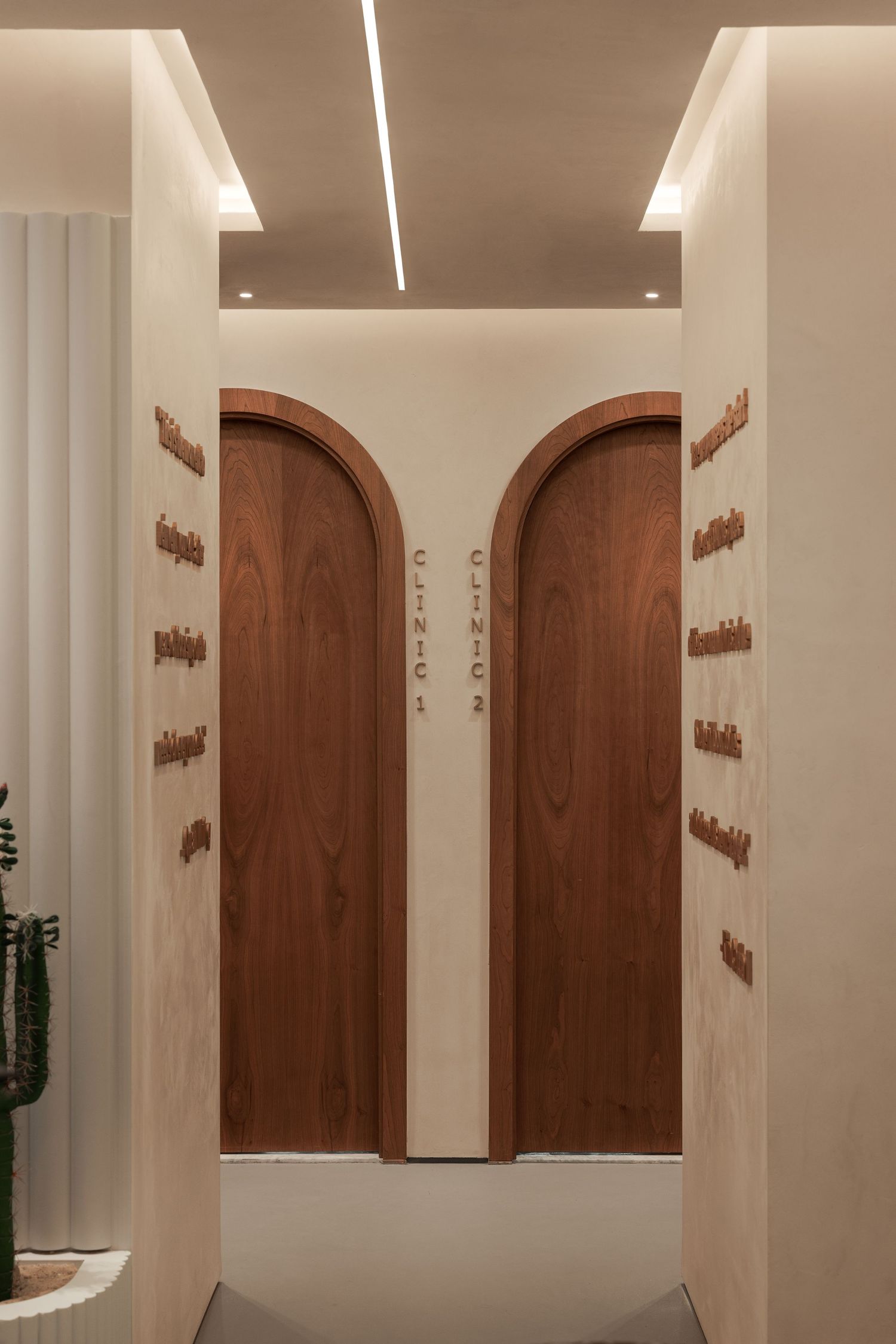 Elegant clinic corridor with twin arched walnut doors labeled Clinic 1 and 2, warm lighting, and cream walls.