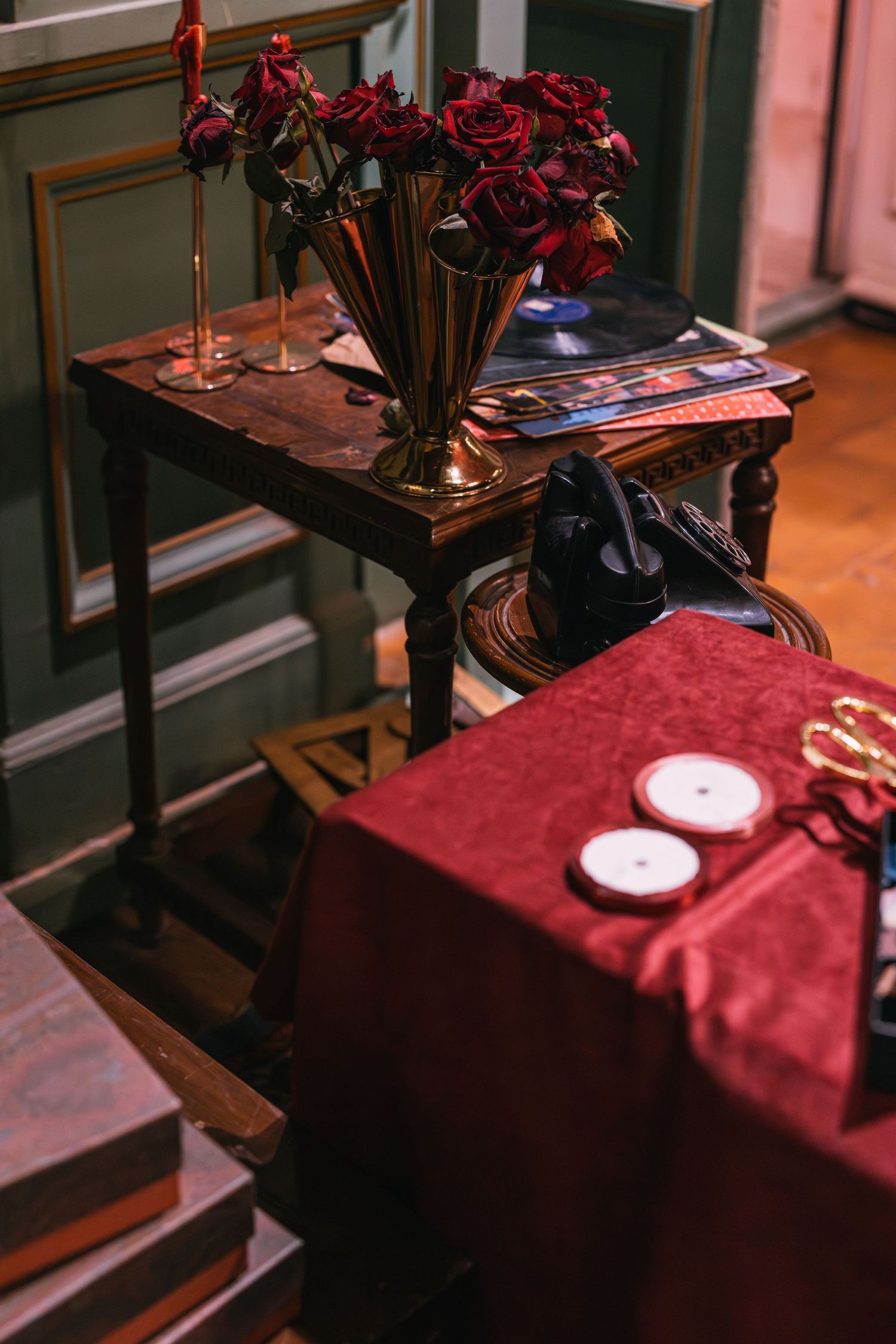 Vintage dark wood table with gold vase of red roses beside a red velvet draped table with candles.