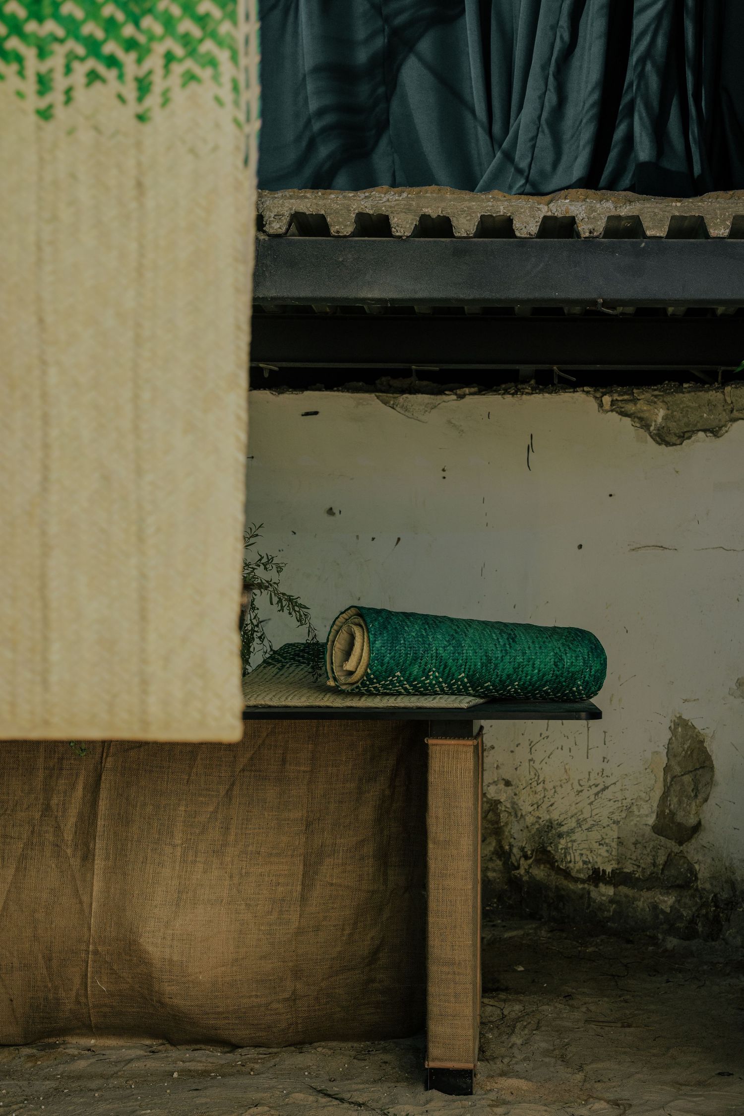 Green woven textile roll resting on a wooden bench in a rustic workspace.