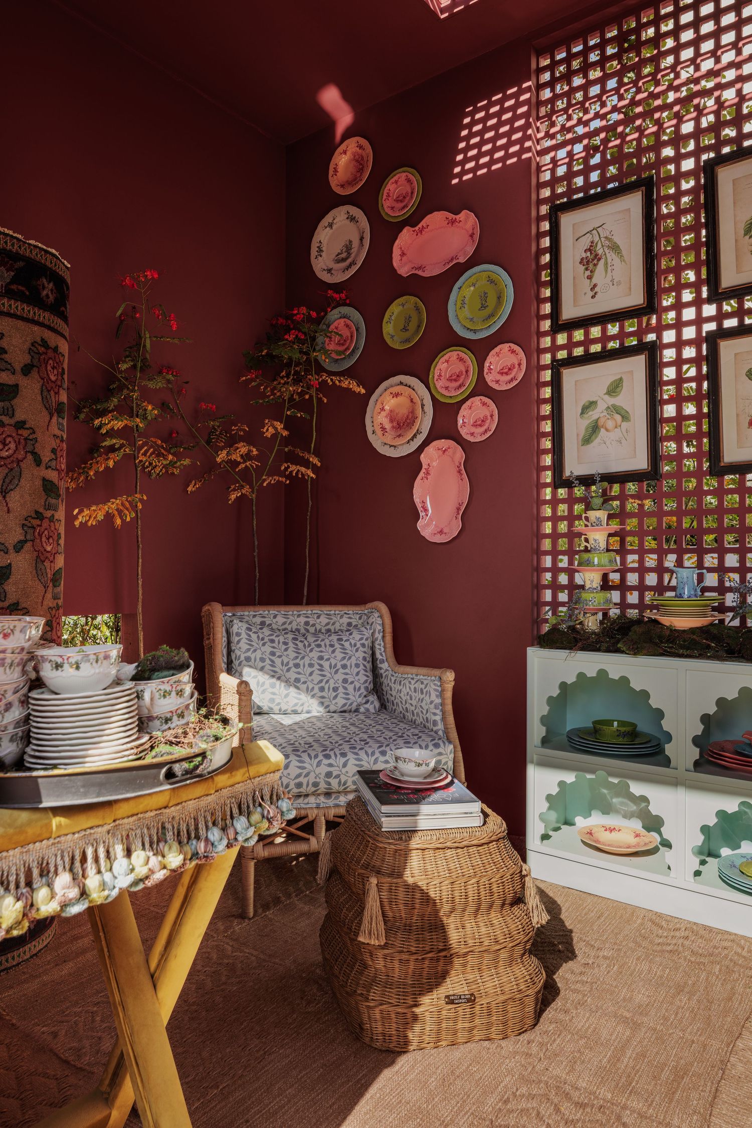 Eclectic dark red room with decorative plates, rattan furniture, and botanical wall art.